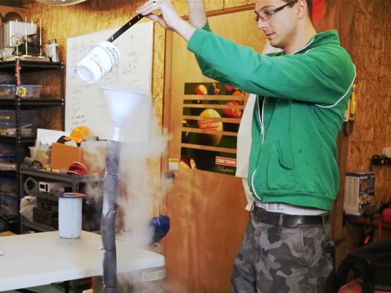 DigiPen RTIS alumus Mikhail Davidov in a lab pouring isopropyl alcohol into a steaming funnel mounted on a pipe.