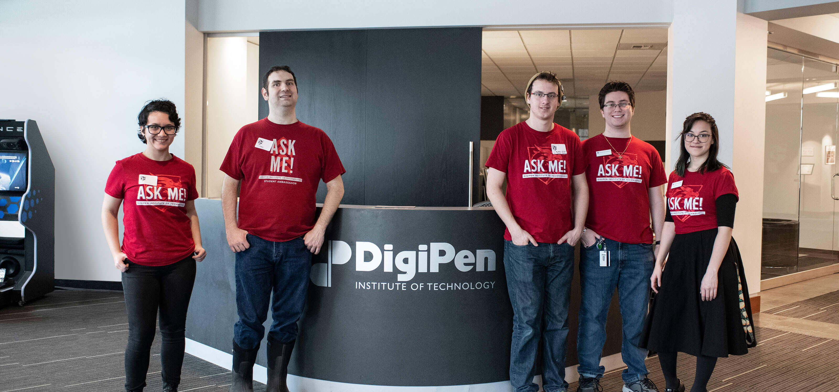 Five people in red t-shirts stand in front of a black desk with DigiPen Institute of Technology written in white letters.
