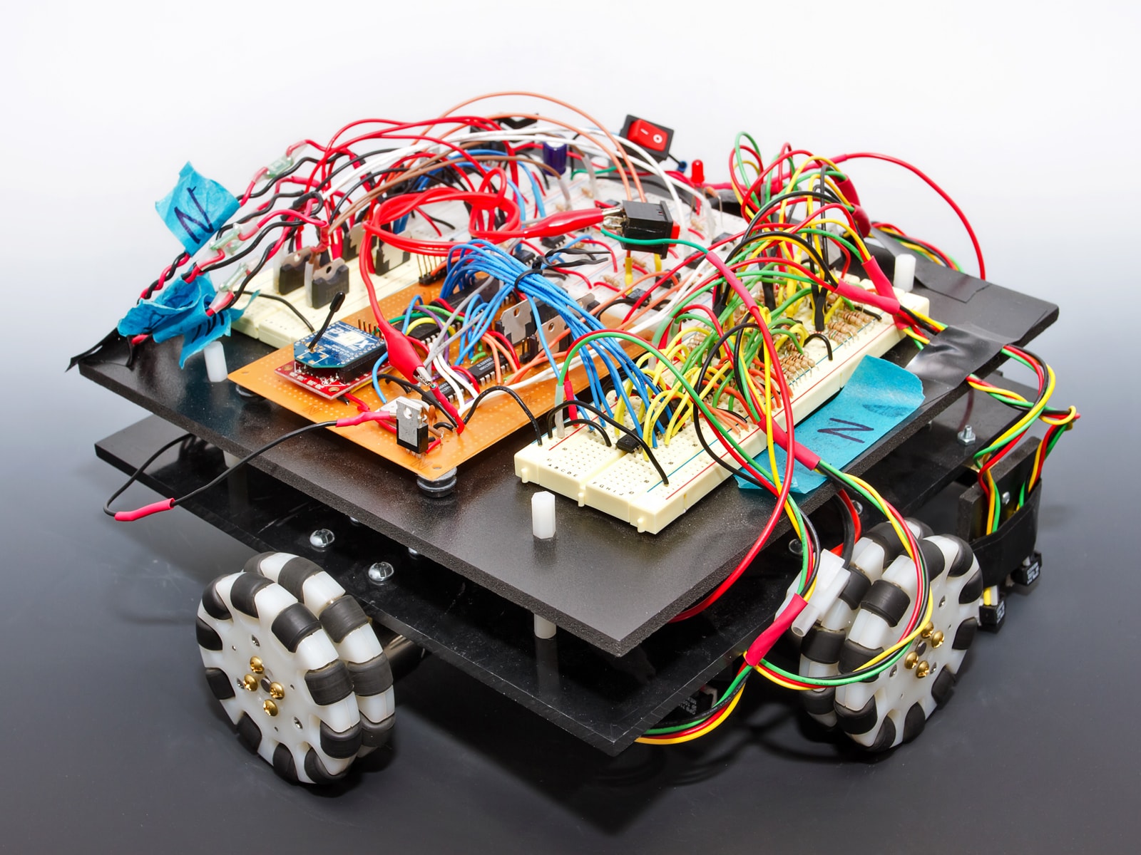 A square robot with exposed circuitry and black and white wheels.
