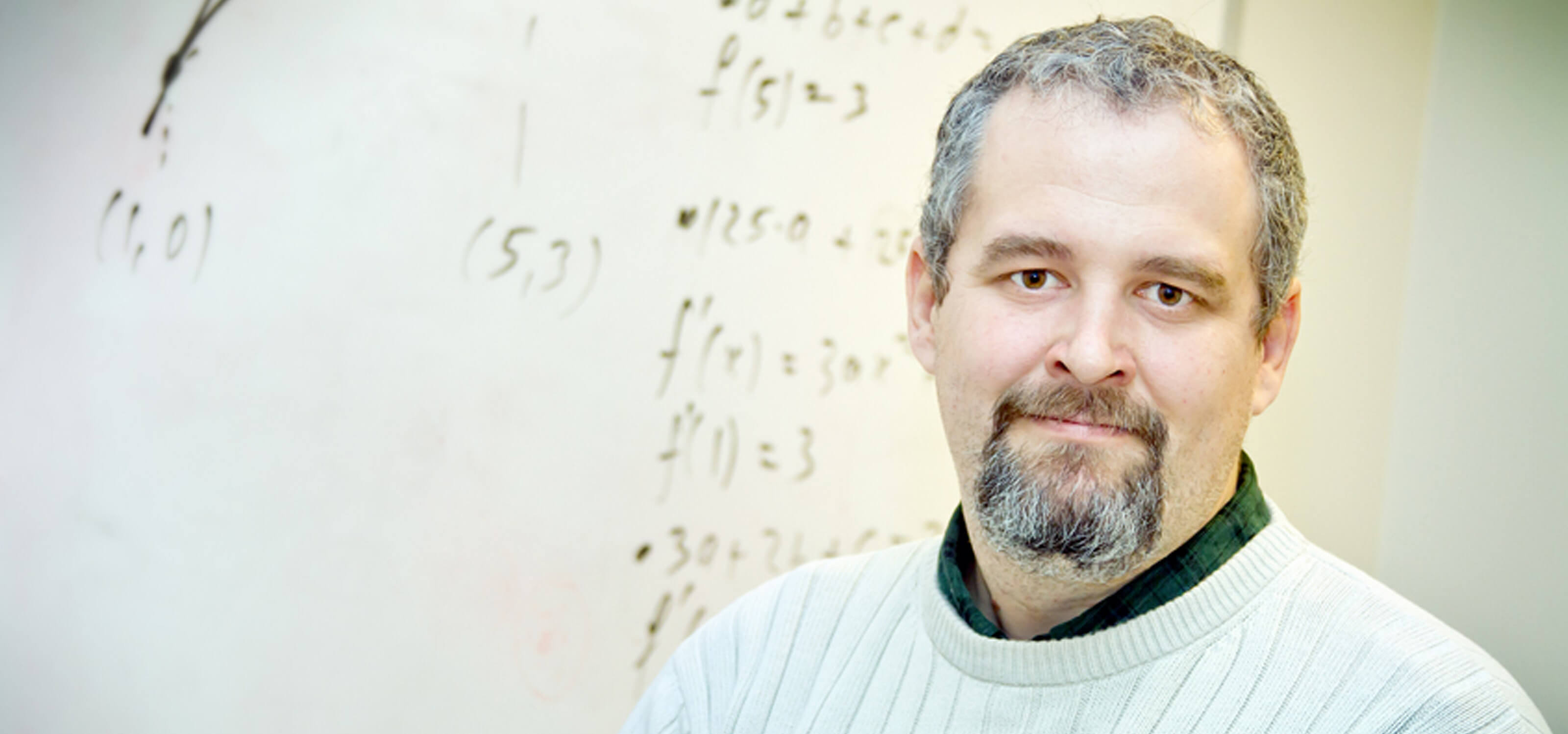DigiPen mathematics professor Barnabas Bede smiling in front of a whiteboard decorated with mathematical formulas