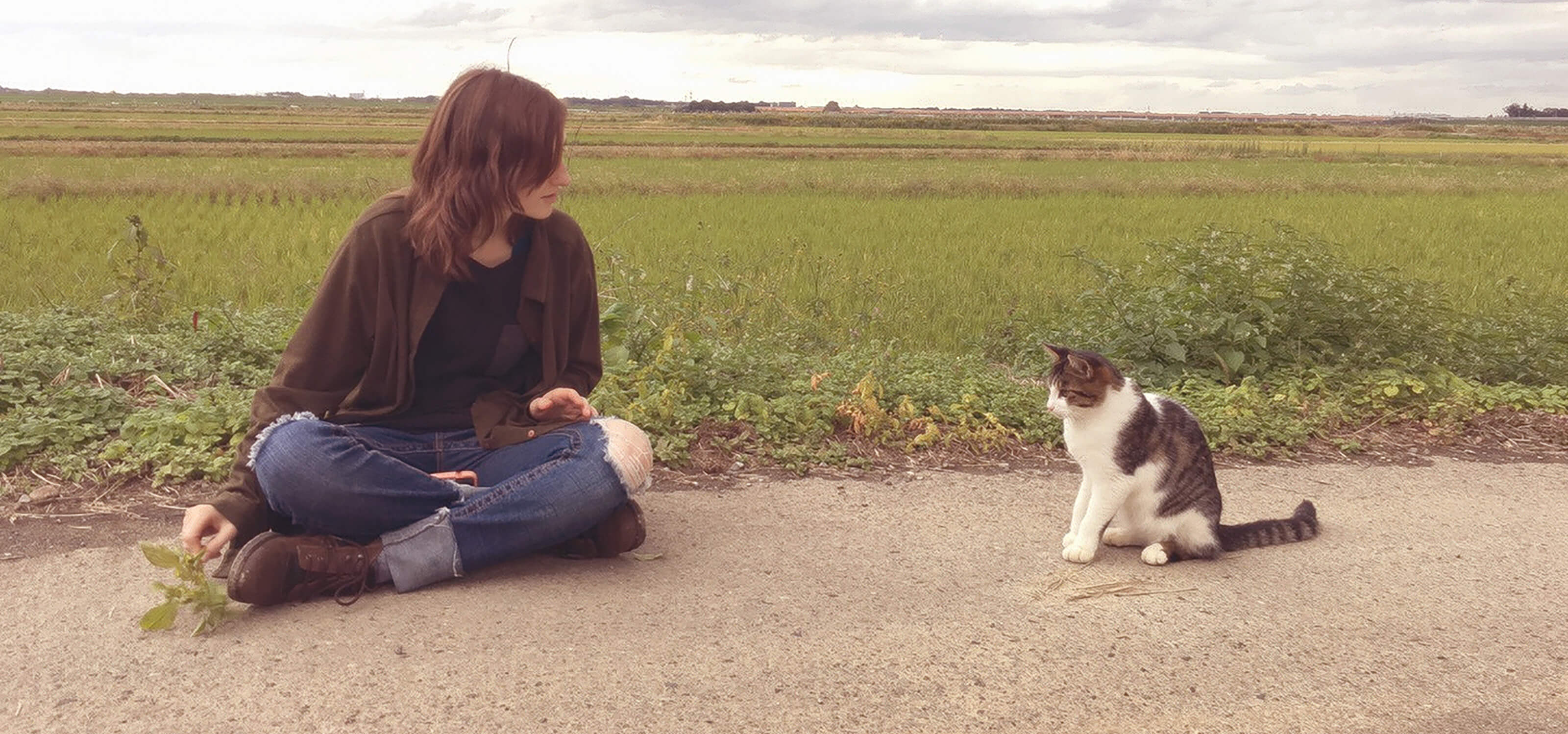 DigiPen alumna Heather Gross sitting on a dirt road in Japan, trying to coax a cat to come over to her