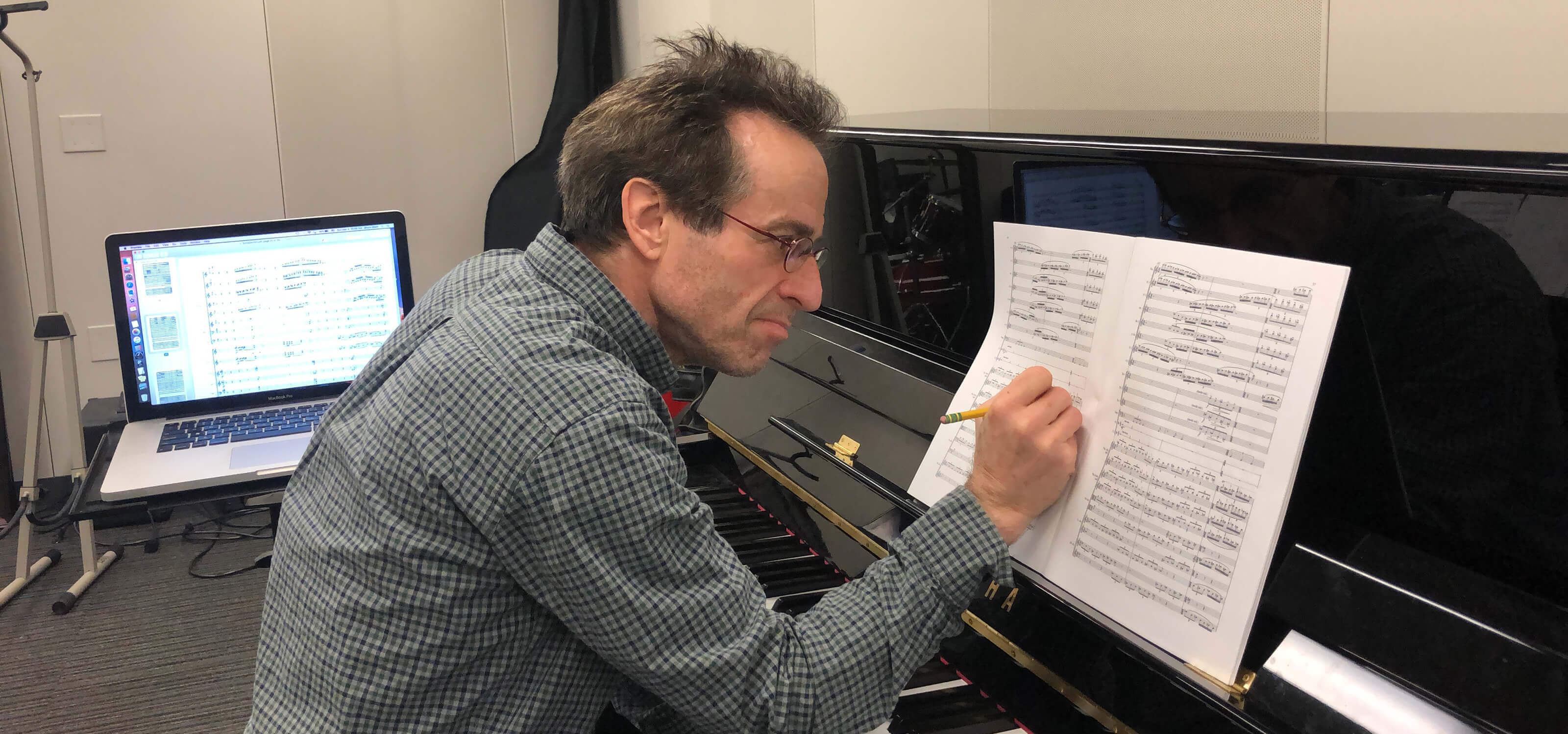 DigiPen music department chair Bruce Stark sitting at a piano, making notations on sheet music