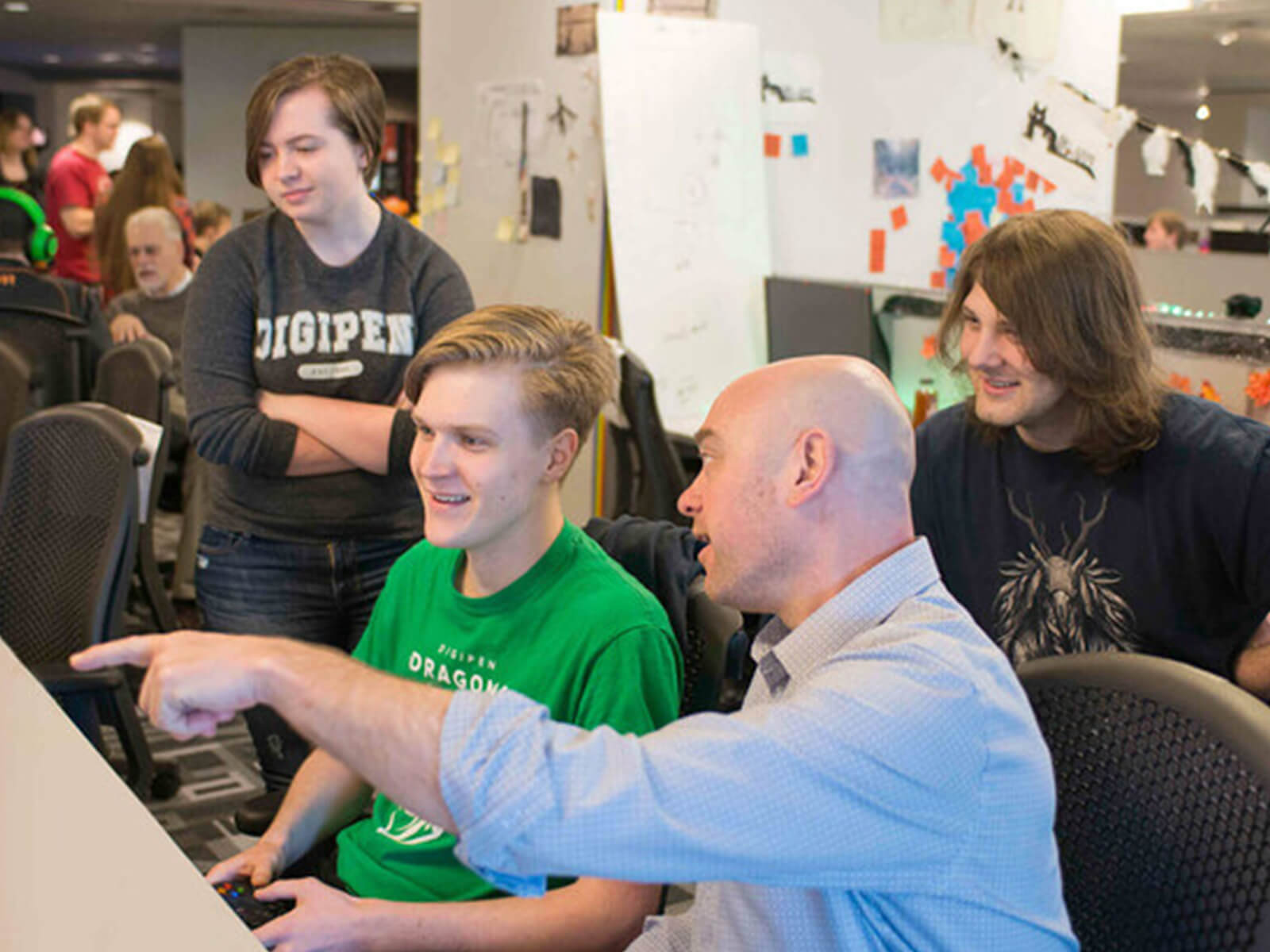 A DigiPen professor points to three students’ game team project on a computer in a campus production lab.