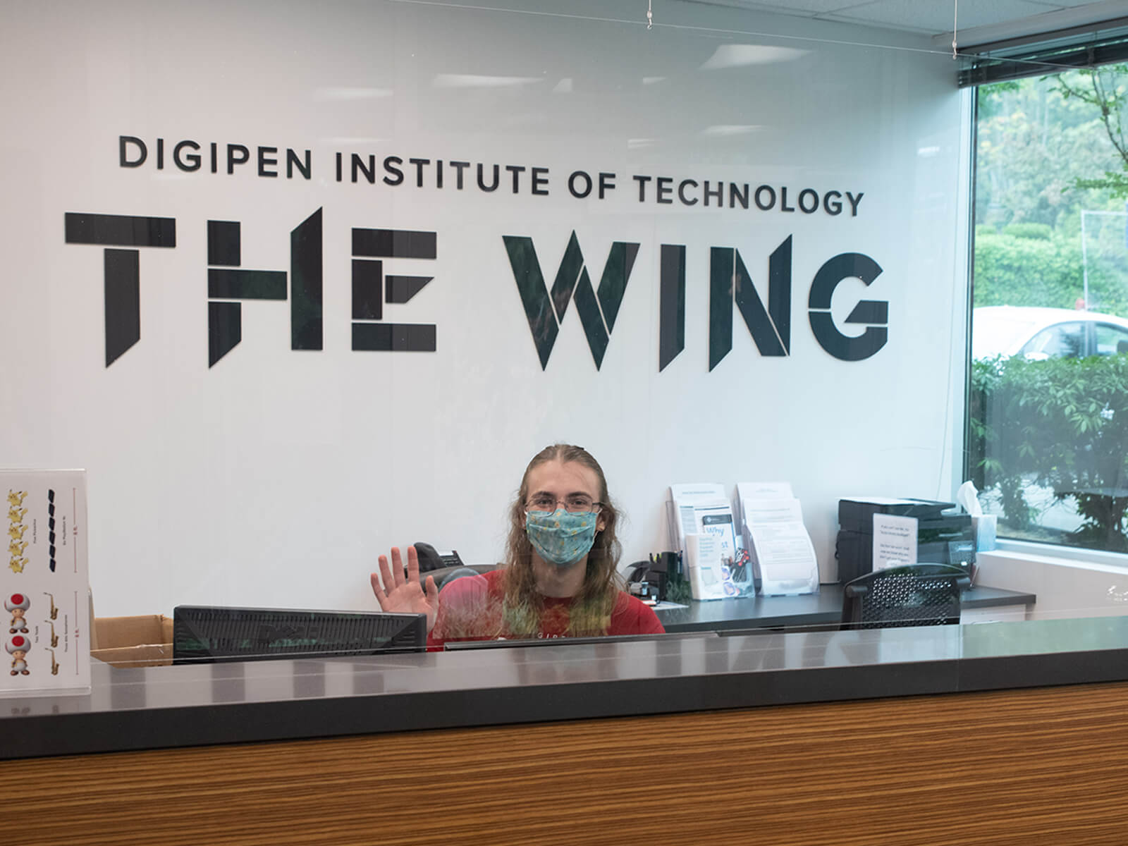 Two masked students wave at the front desk of DigiPen’s new campus expansion, The Wing. 