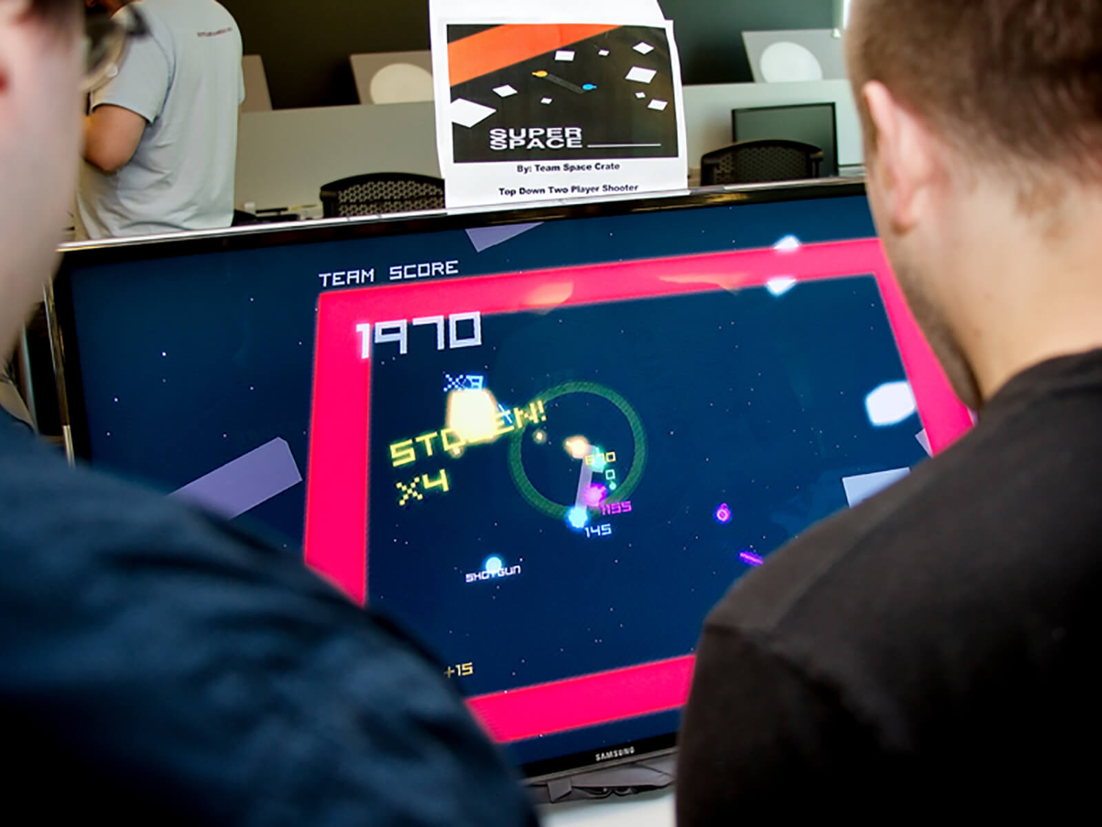 Over-the-shoulder view of two people playing the game Super Space ____; blocks and numbers float in space on a TV screen