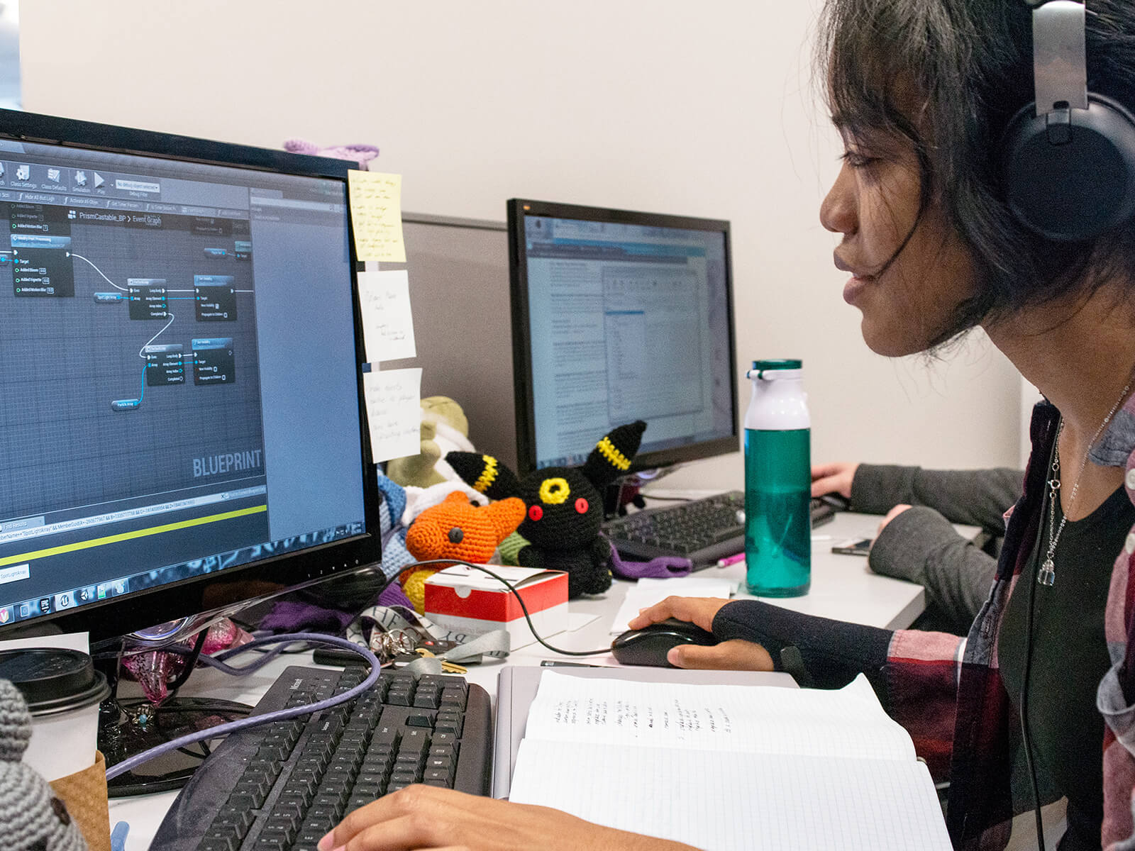 A DigiPen game design student works on her computer surrounded by knit plush toys.