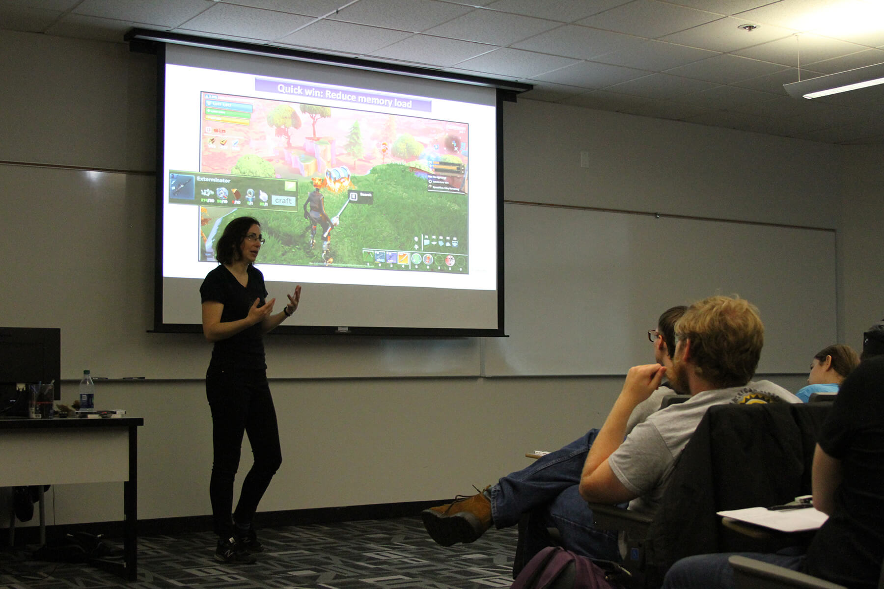 Dr. Hodent gestures towards students during her lecture, with scenes from a Fortnite play test projected behind her. 