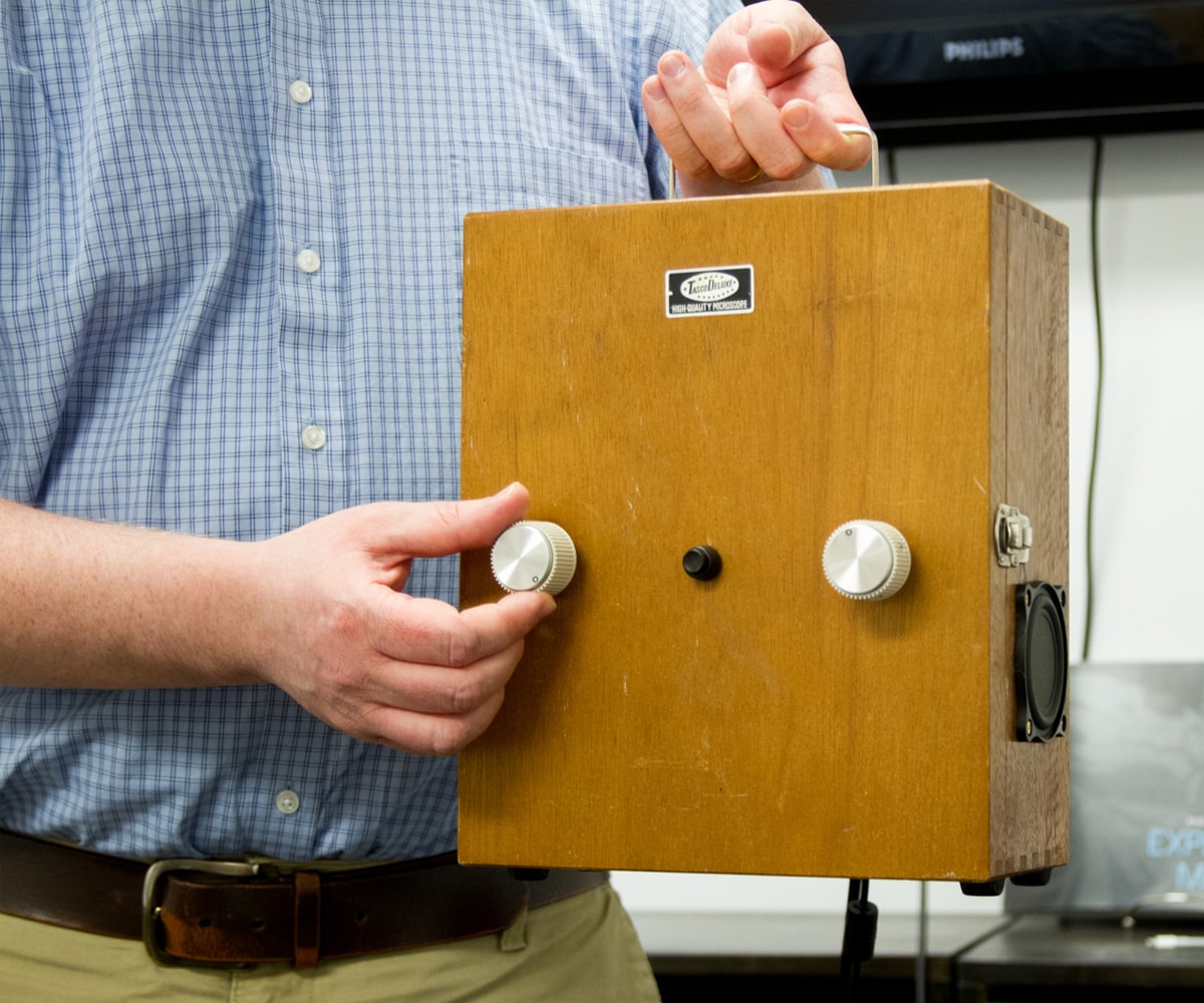 Greg Dixon shows off his Space Regenerator, a small wooden box with two knobs on the front and a speaker on the side