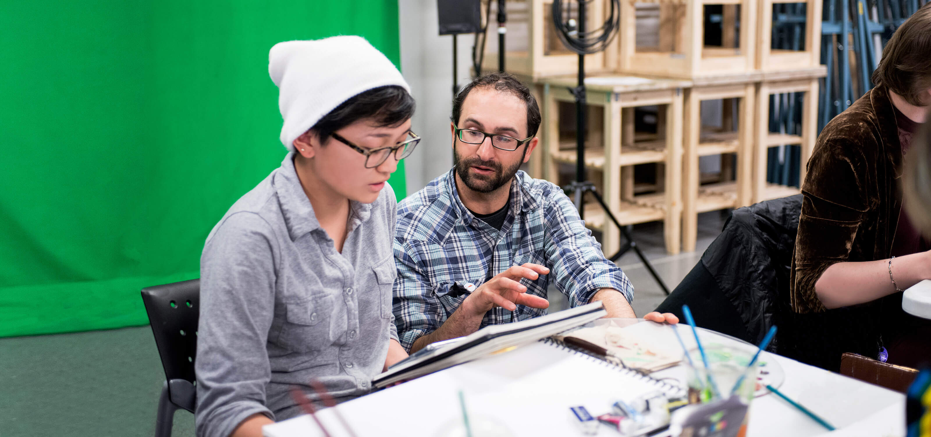 A DigiPen faculty member works with a student, a green screen behind them