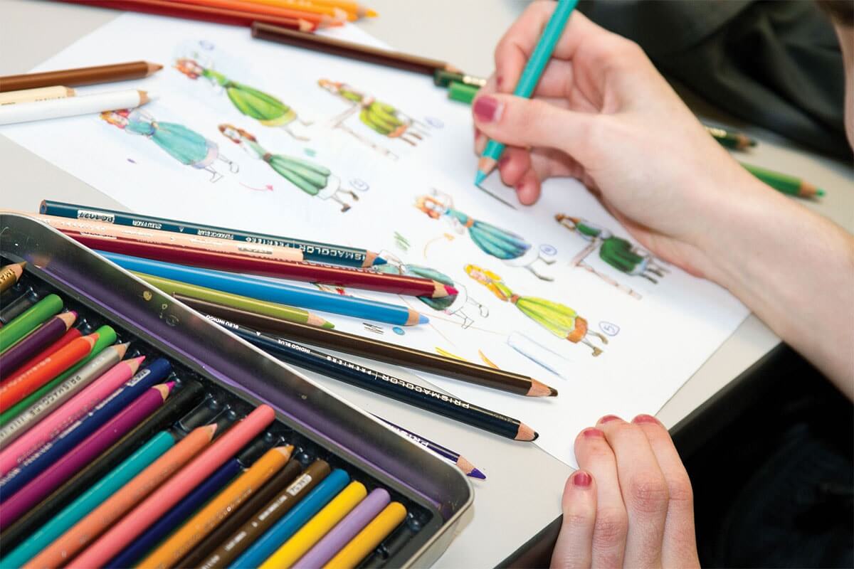 Close-up view of a DigiPen student sketching various female characters with colored pencils in the foreground