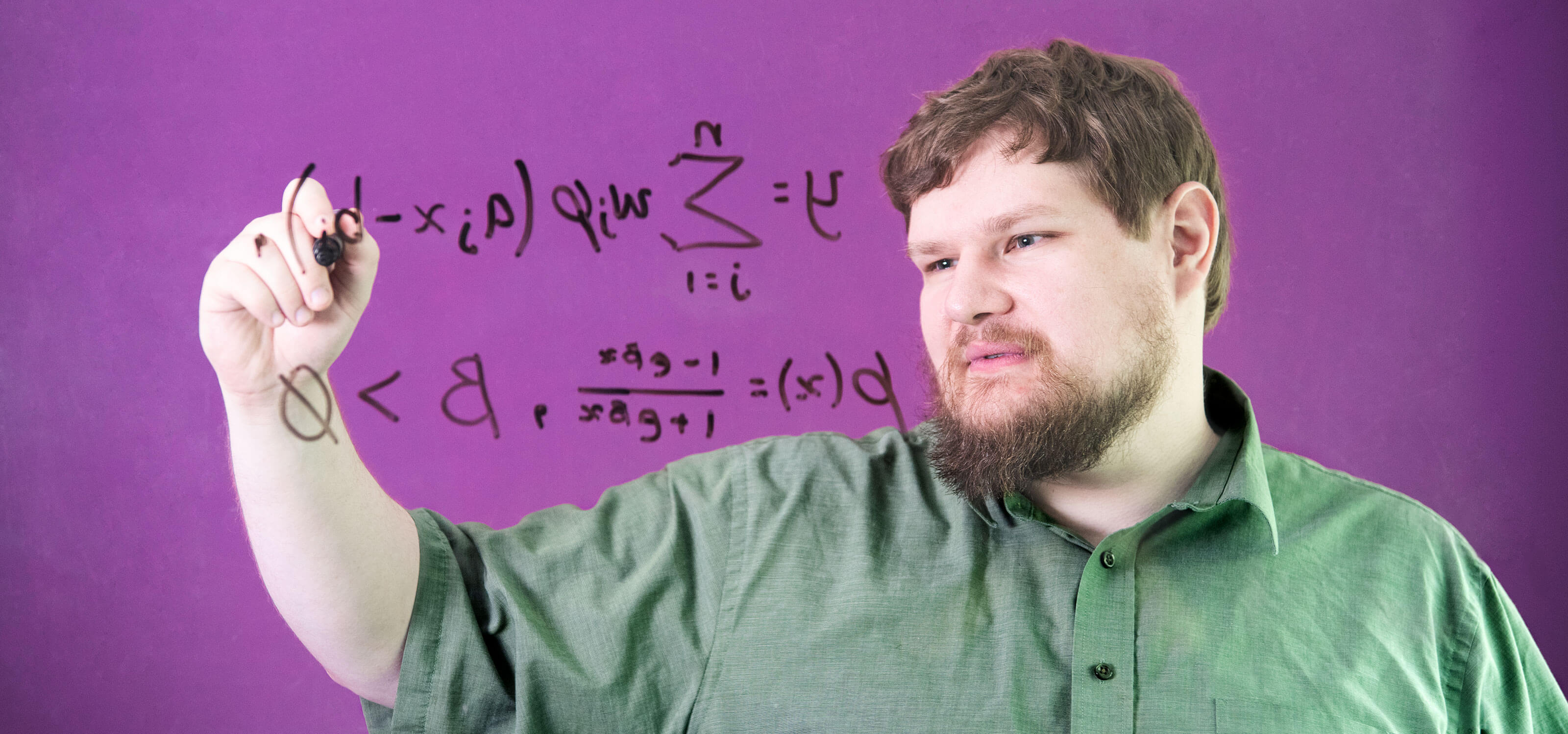 Student uses a black marker to write an algorithmic formula on glass in a DigiPen classroom.