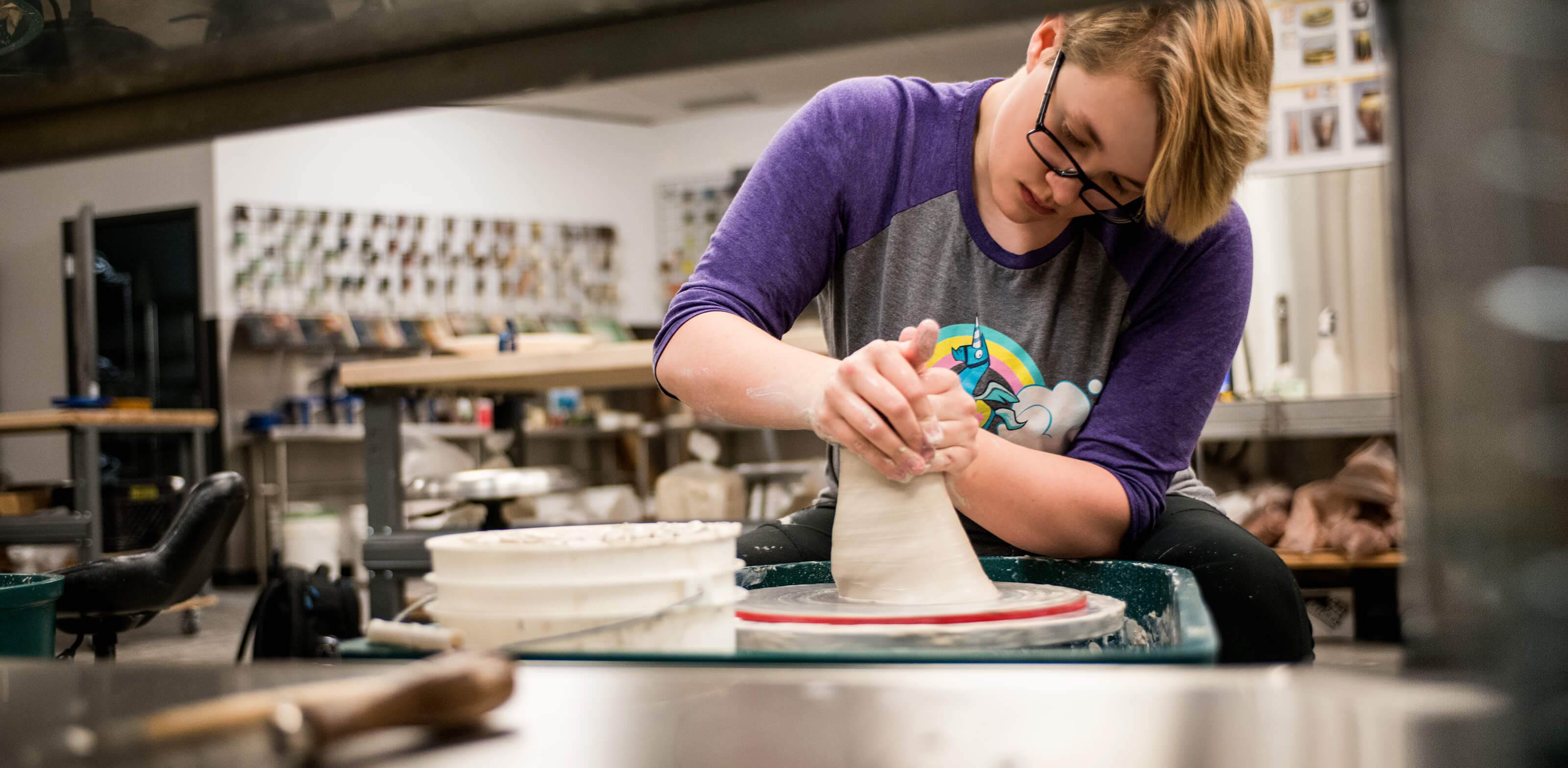 A student concentrates as she molds clay on a spinning wheel