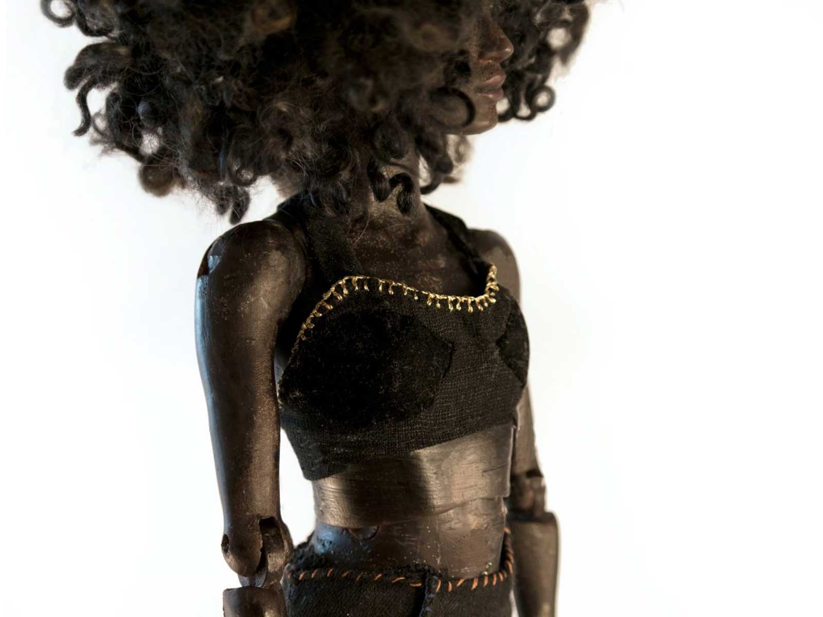 A female doll with voluminous curly hair wearing a gold trimmed halter top.
