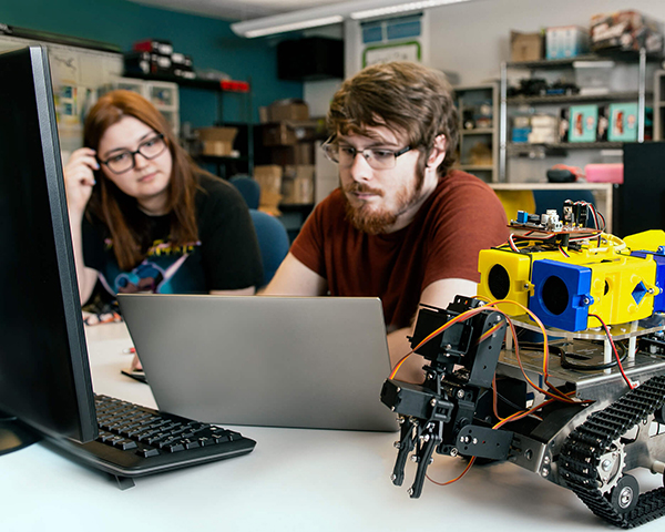 DigiPen engineering students sit next to an self-navigating robot.