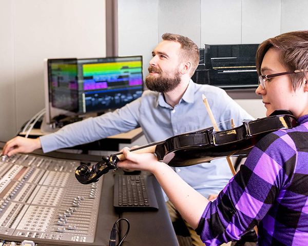 A DigiPen student plays violin next to a large audio mixing board.