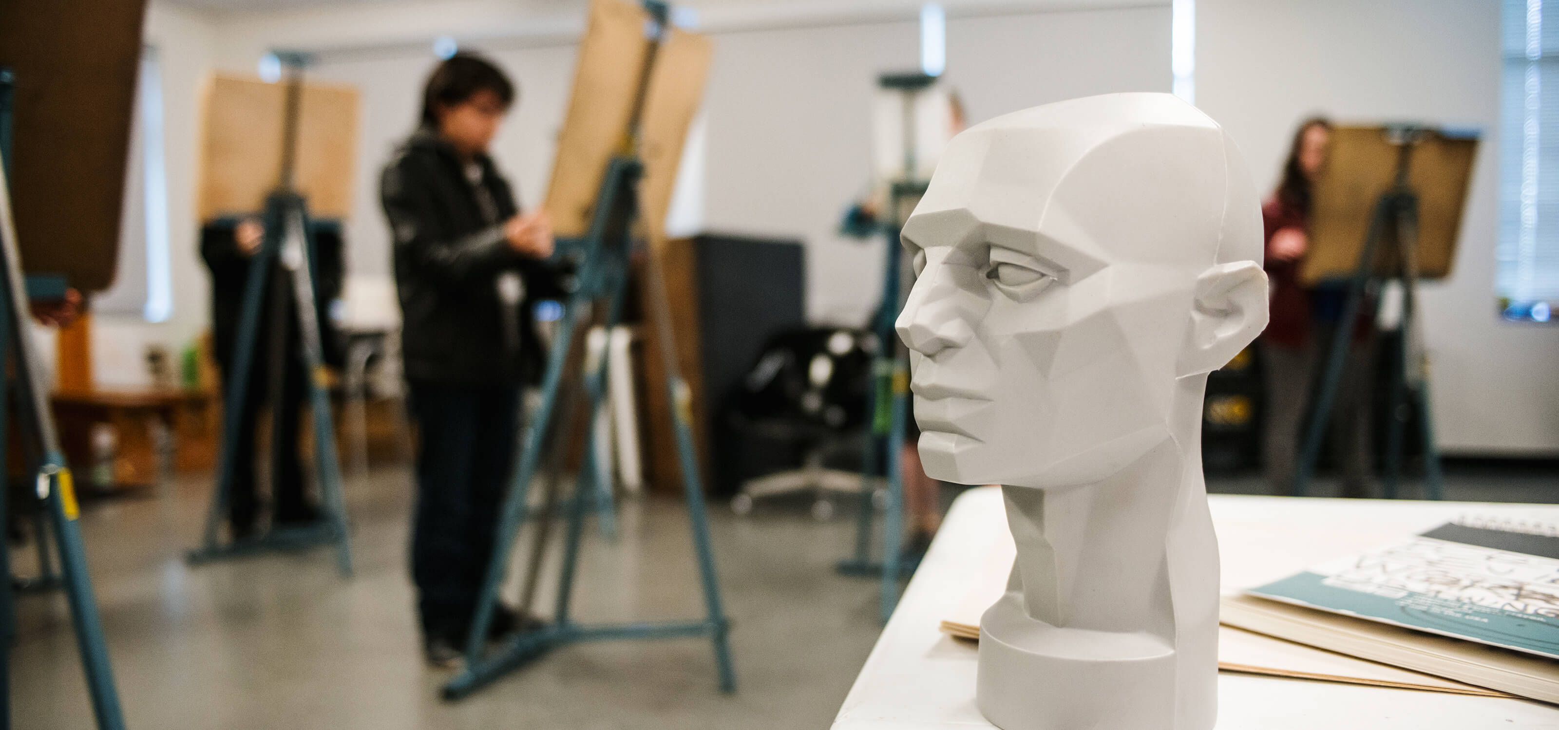 A sculpture of a head in the foreground, with students at easels in the background