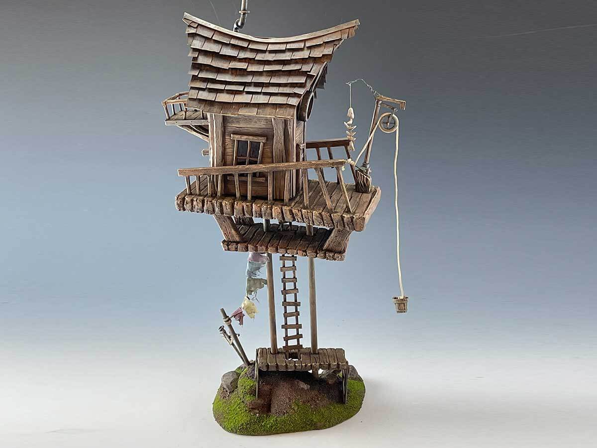Model of a small house precariously standing on two wooden pillars.