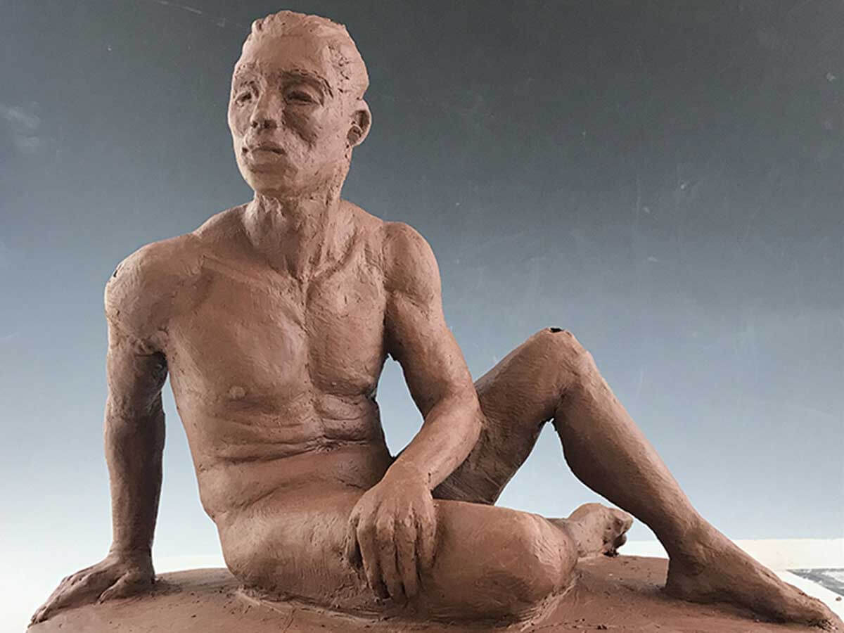 Clay model of a nude man sitting on the floor.