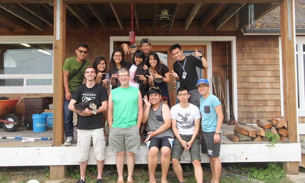 OIP students with staff and Redmond students pose in front of a wooden building