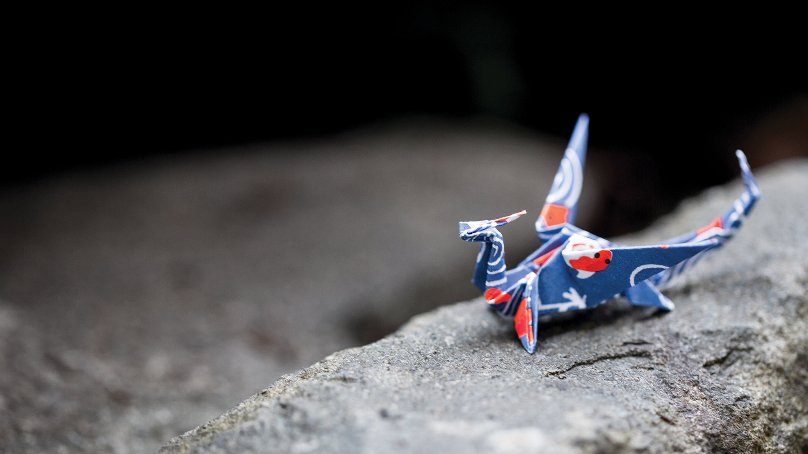 A dragon crafted from blue origami paper sitting on a rock