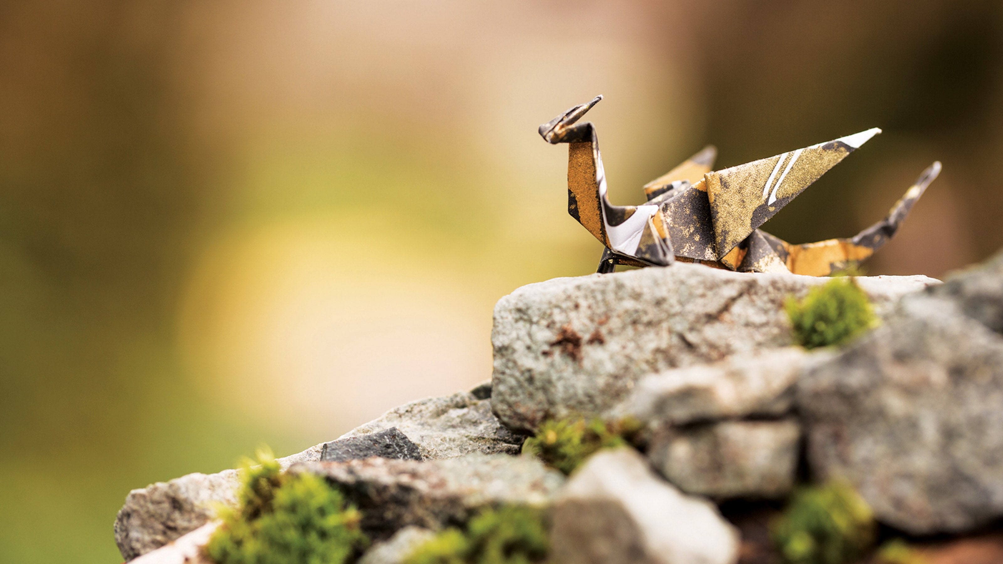 A gold and black origami dragon sitting on a mossy rock against a green background