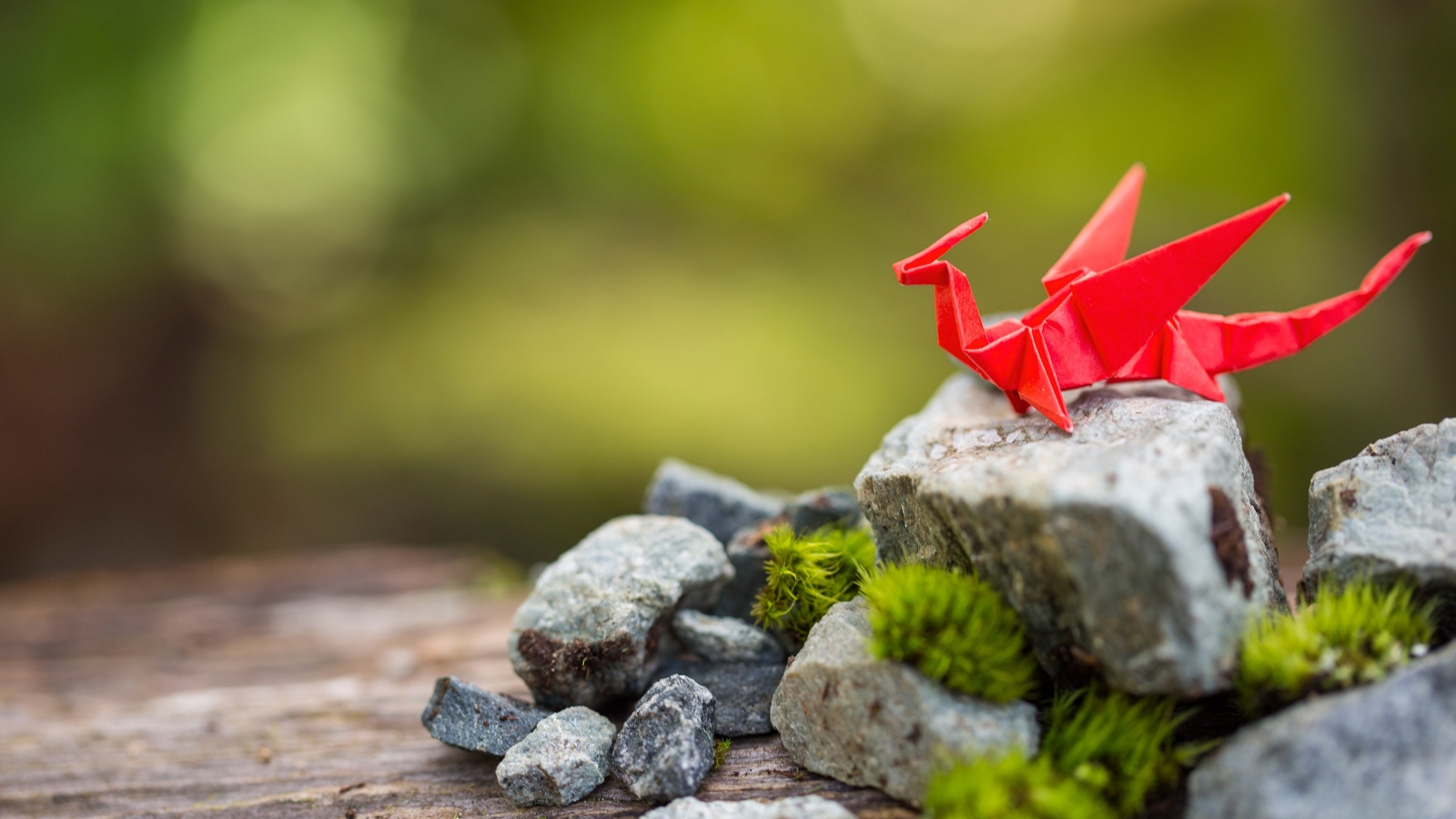 A dragon crafted from red origami paper sitting on a mossy rock