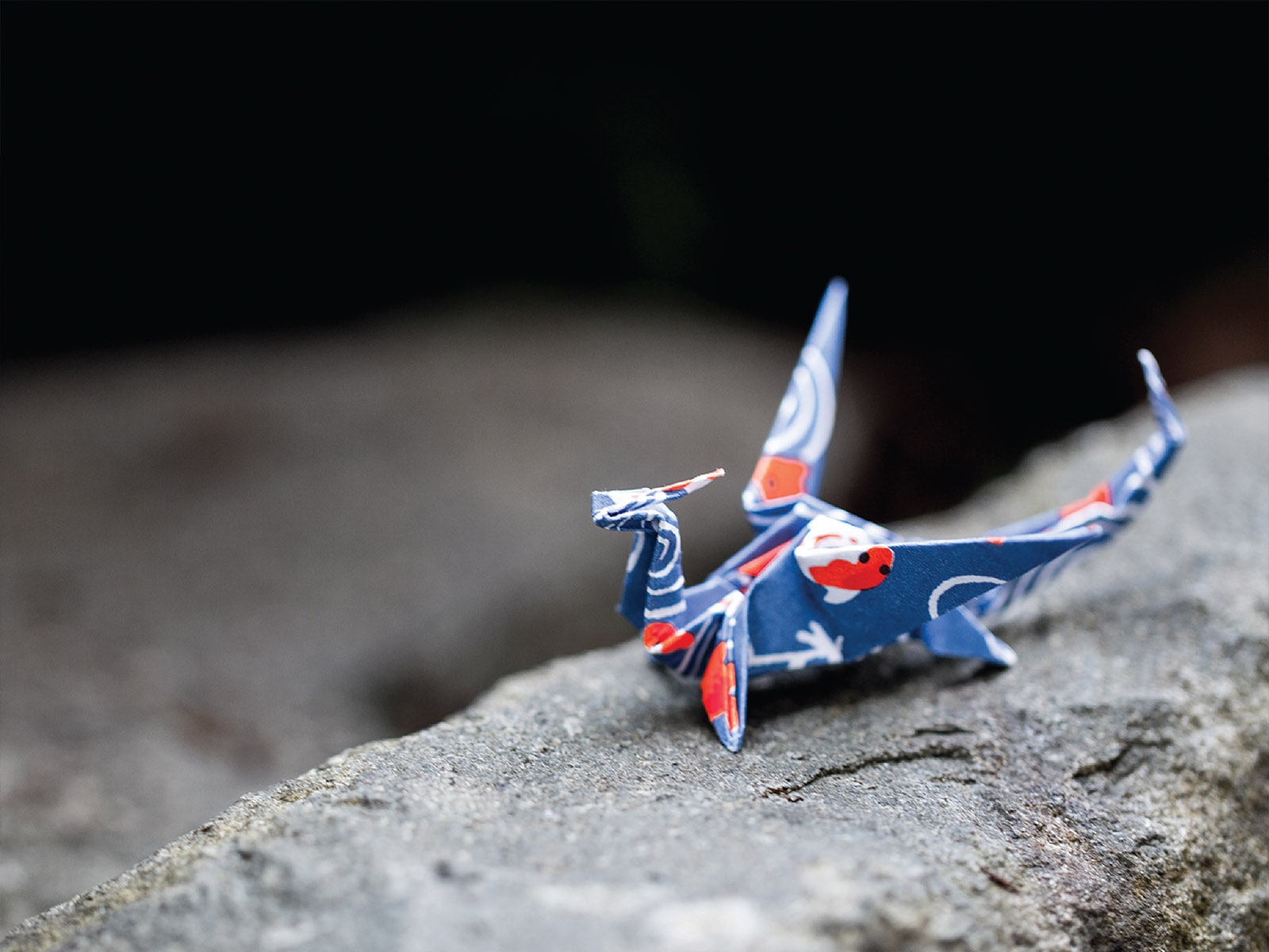 A dragon crafted from blue origami paper sitting on a rock