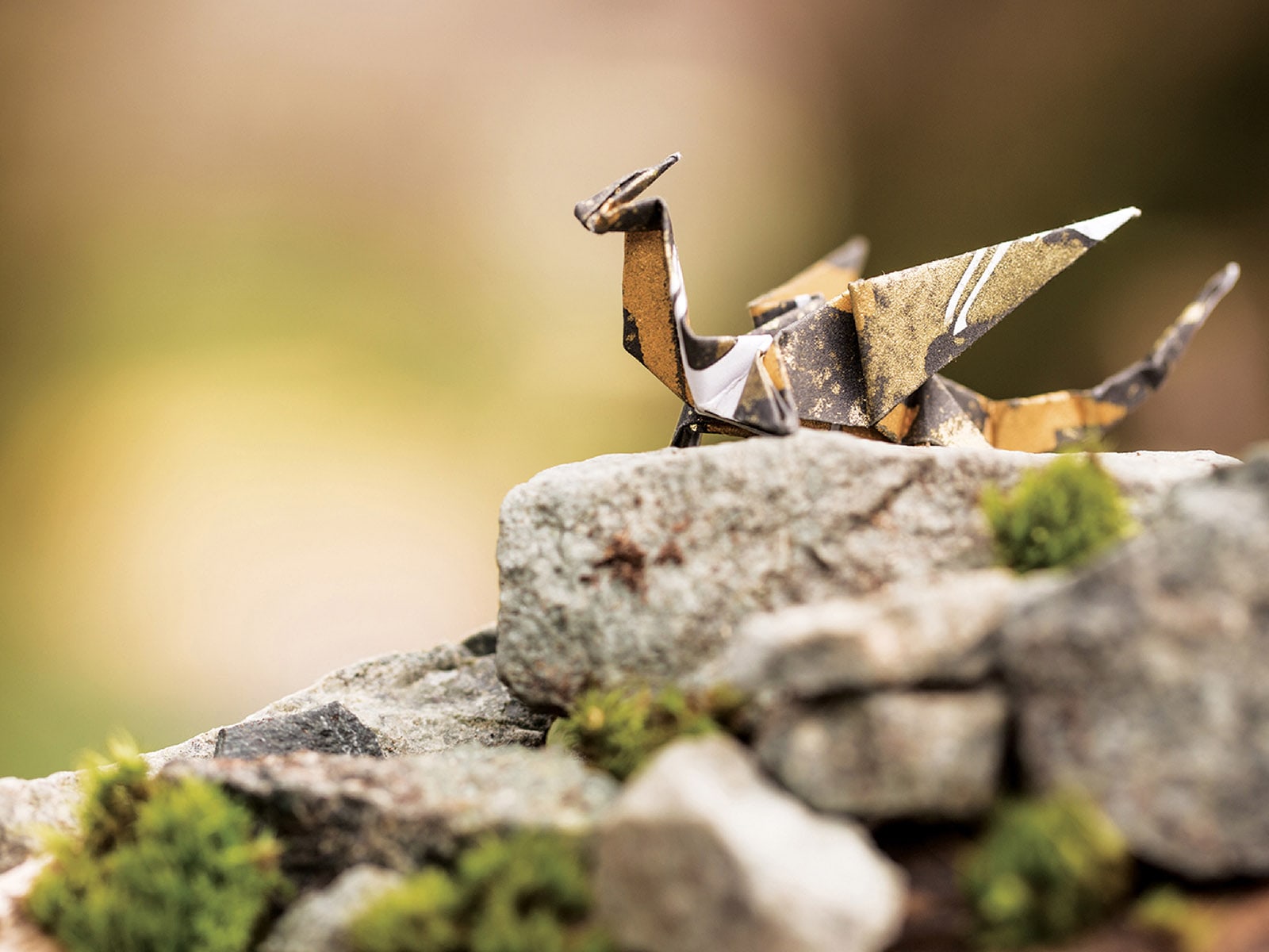 A gold and black origami dragon sitting on a mossy rock against a green background