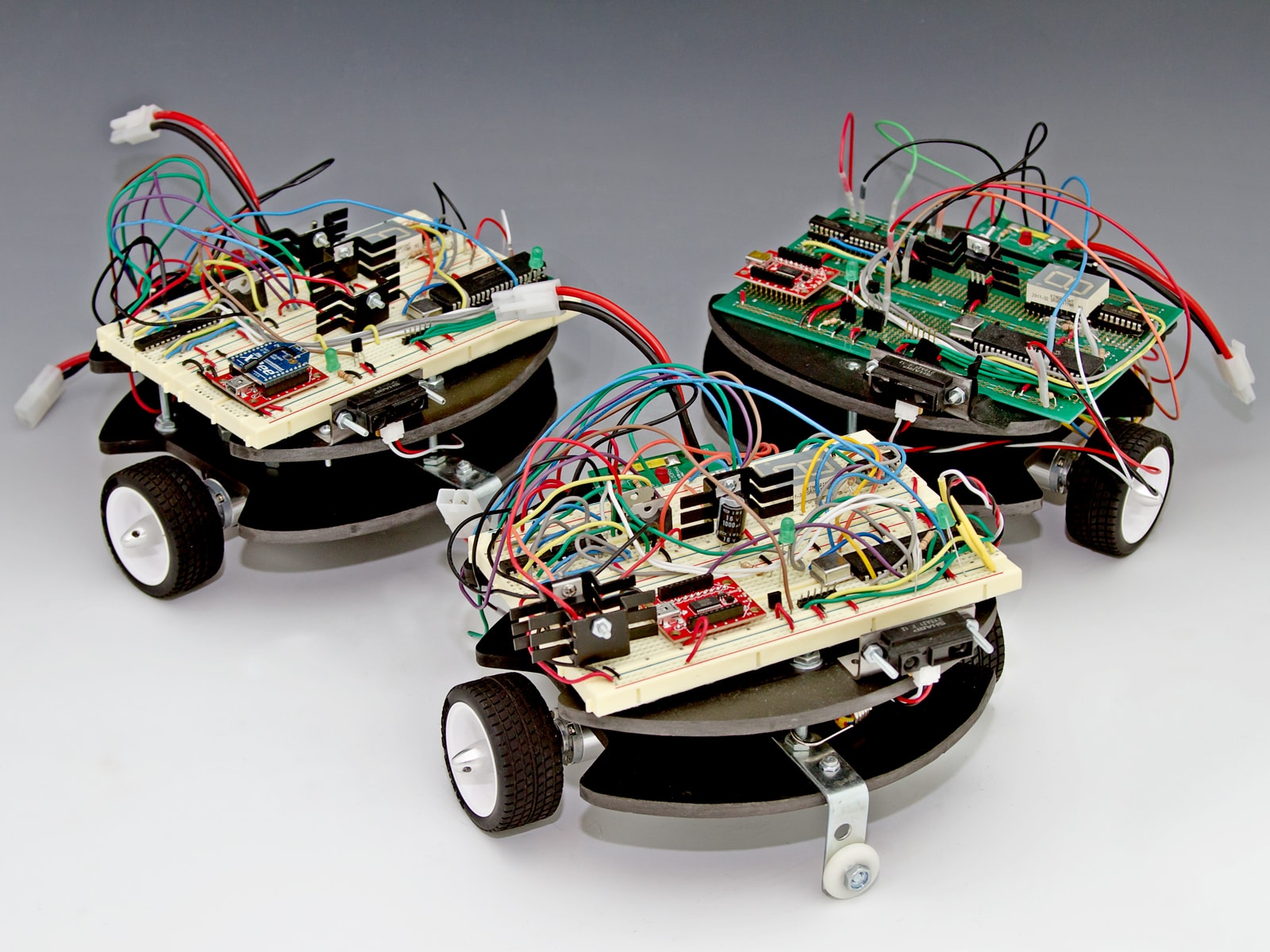 Three square robots with rounded fronts, black and white wheels and exposed circuitry.