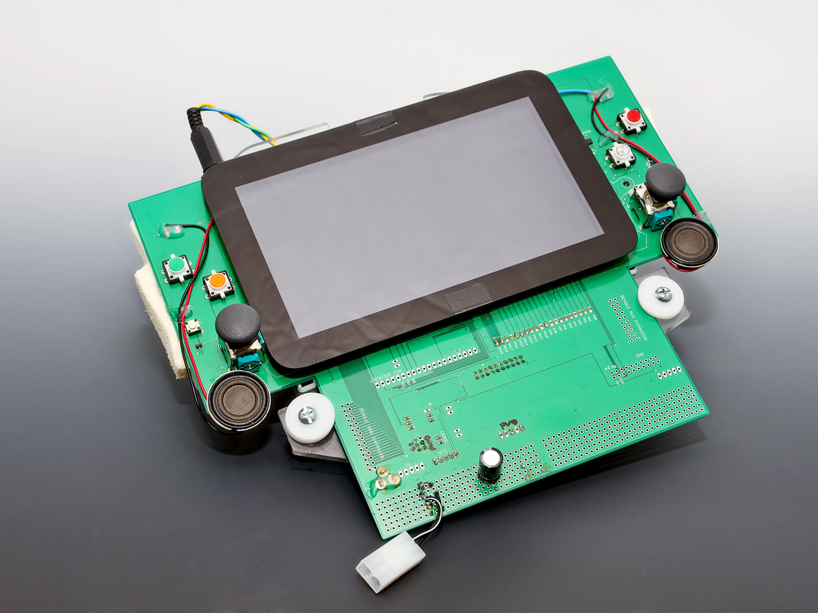 A screen mounted to a green circuit board with two control sticks.