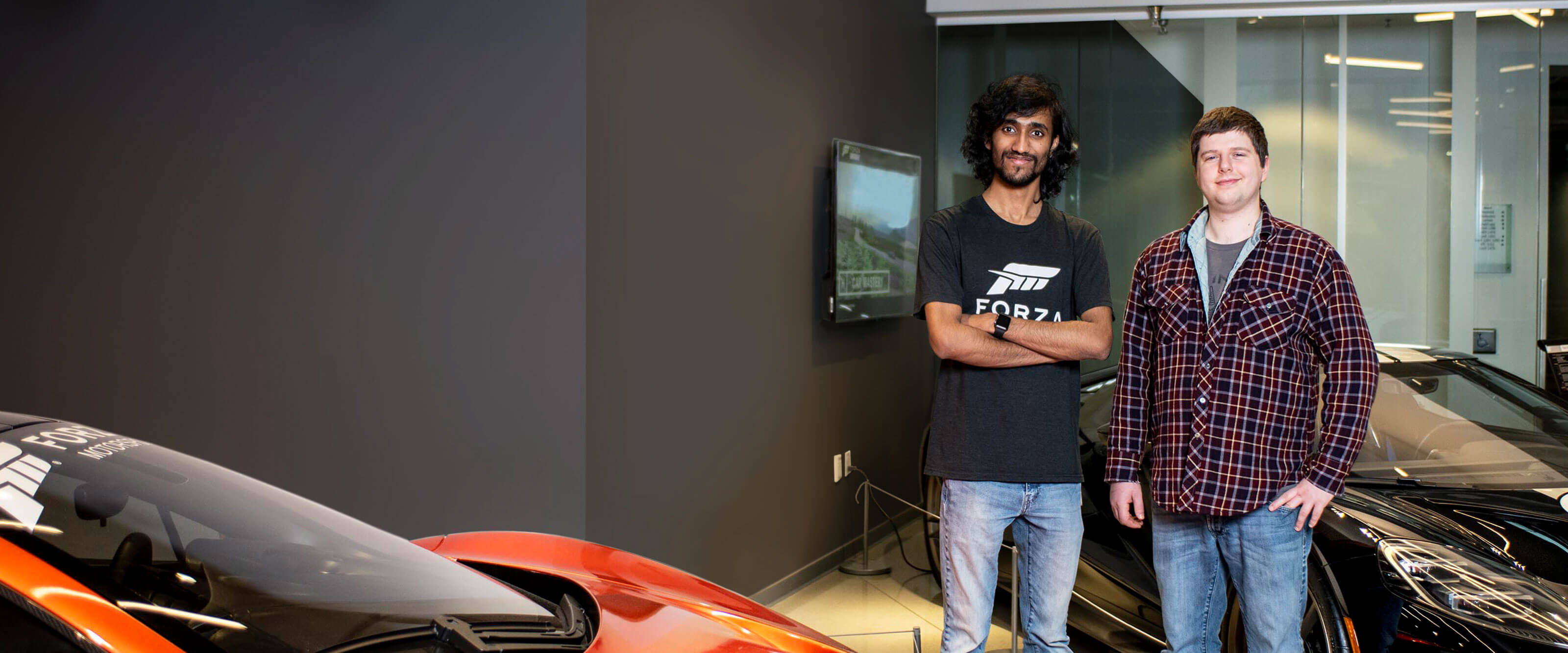 Michael Pitaniello and Deepak Chennakkadan stand next to luxury cars in the Turn 10 Studios lobby.