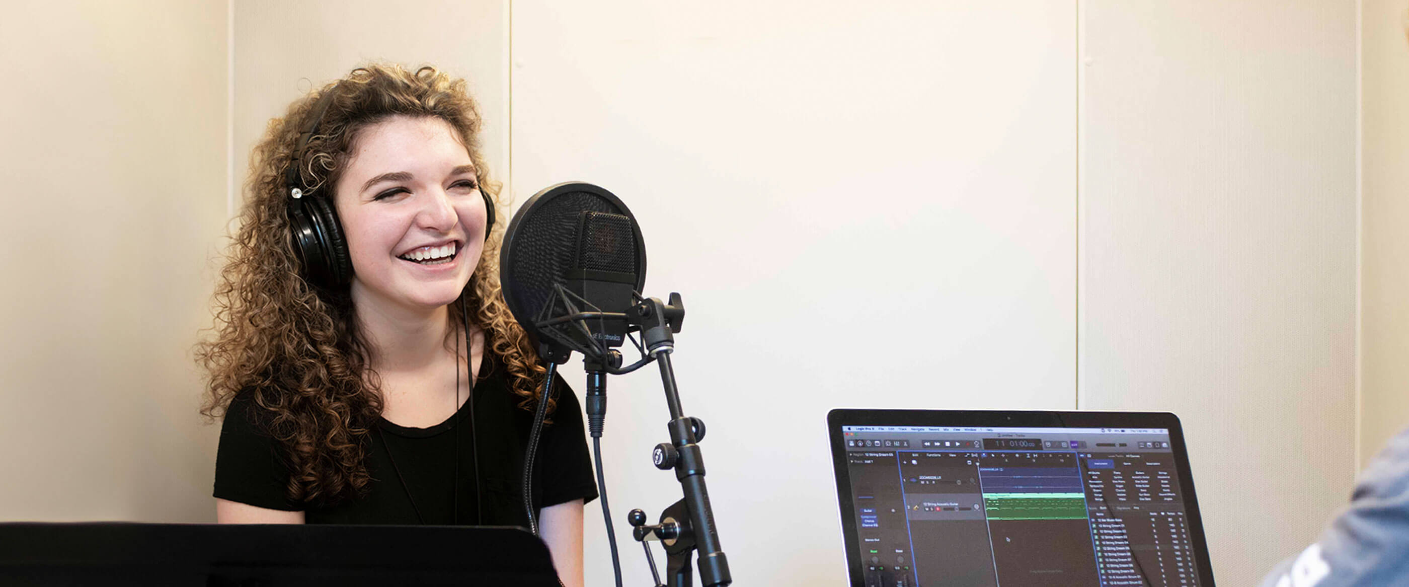 Woman stands in front of microphone next to a computer.