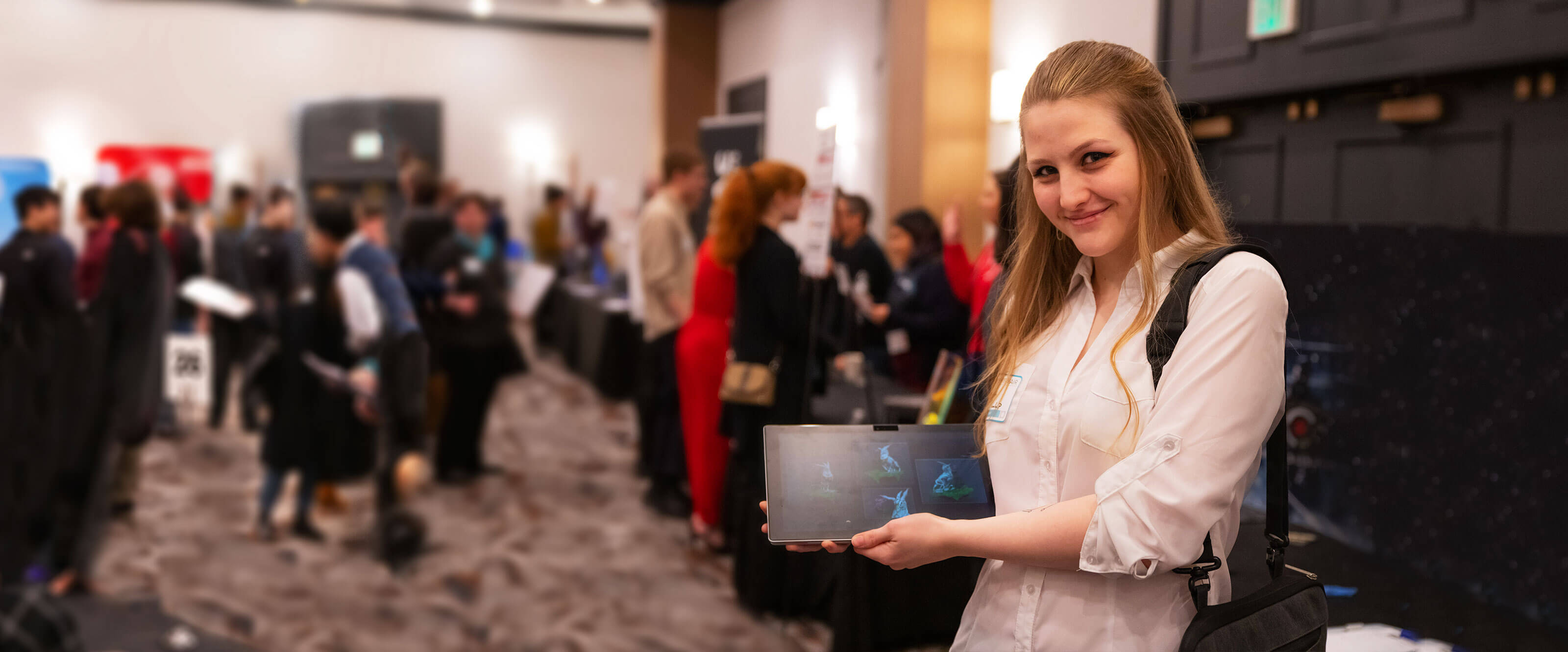 A DigiPen student presents her artwork on a tablet during a busy internship fair.