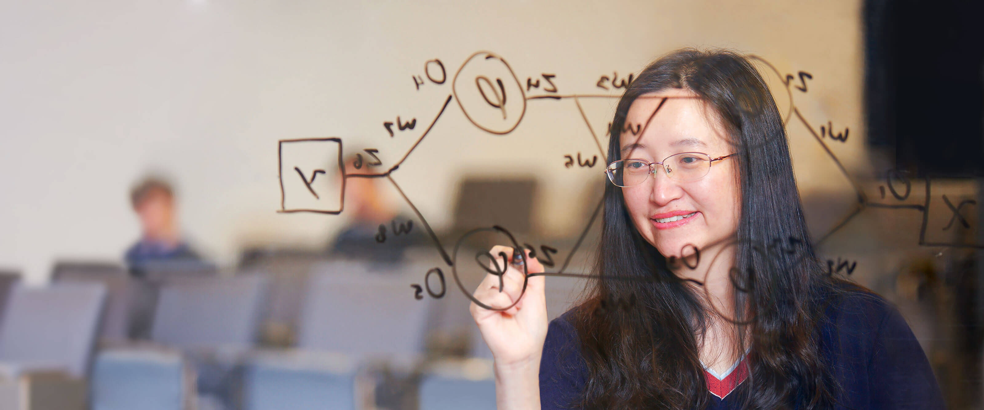 Student uses a black marker to draw a neural network map on glass in a DigiPen classroom.