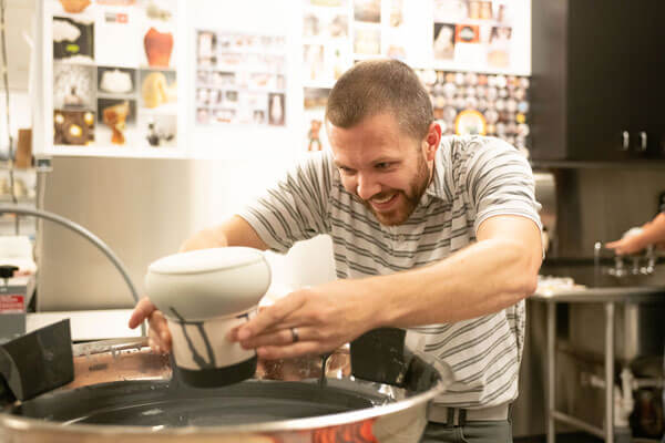 A man focuses intently as he dips a piece of kiln-fired pottery into a bowl of glaze.