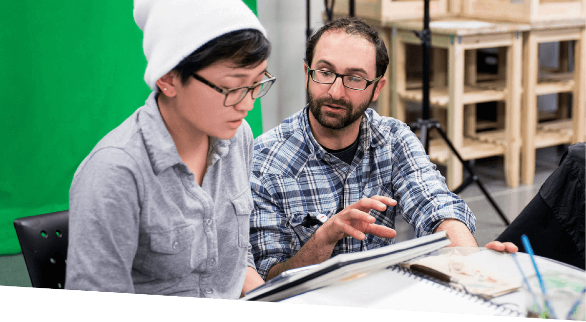 A DigiPen faculty member works with a student, a green screen behind them