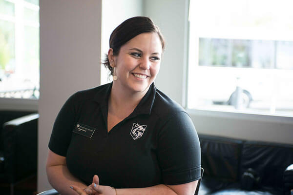 A seated, smiling woman in a black DigiPen Dragons polo shirt looks offscreen to the right.