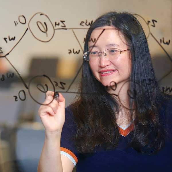 A DigiPen student stands smiling while drafting a neural network on a piece of glass