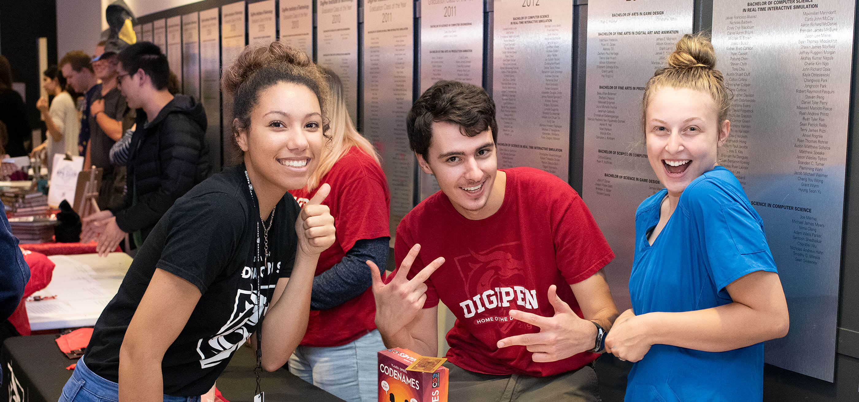 DigiPen students smile with a thumbs up and peace signs.