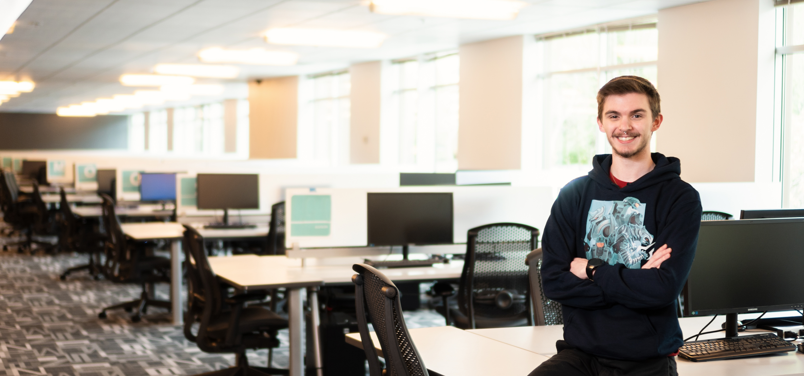 DigiPen Student of the Year Brandon Stam poses with their arms crossed in the campus lab.