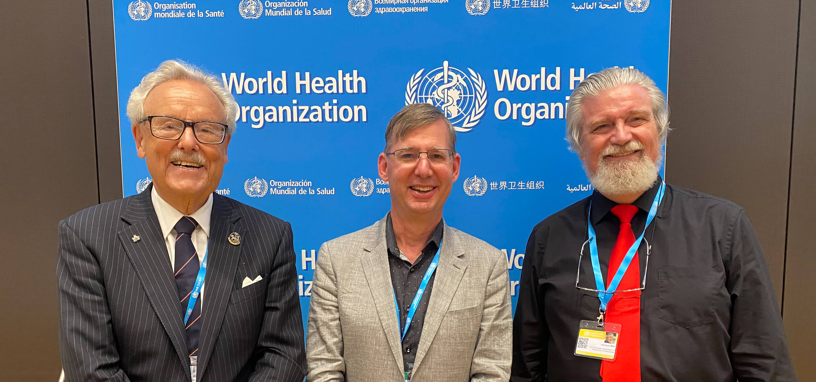 Brian Schmidt poses with two other summit attendees in front of a blue World Health Organization banner. 