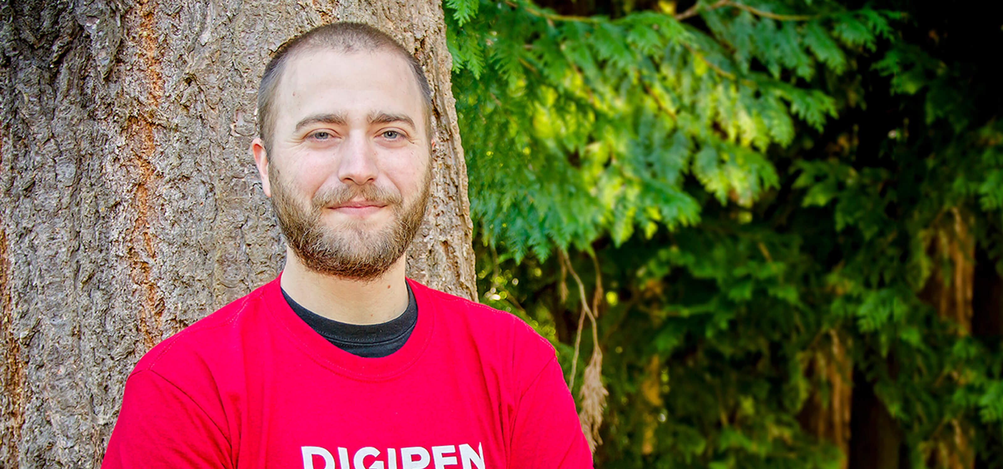 DigiPen student Casey Donelson leaning against a tree on the DigiPen campus with his arms crossed