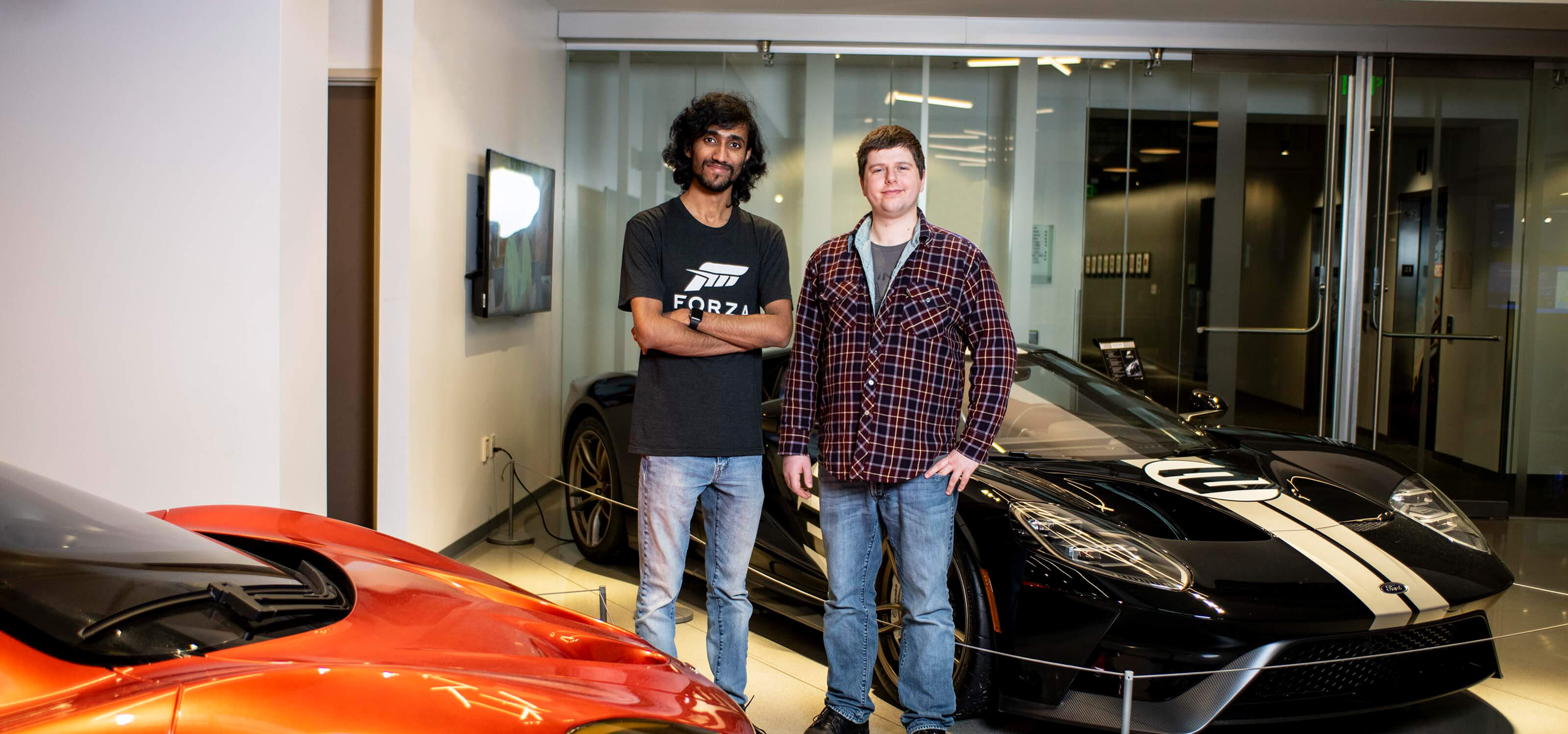 Michael Pitaniello and Deepak Chennakkadan stand next to luxury cars in the Turn 10 Studios lobby.