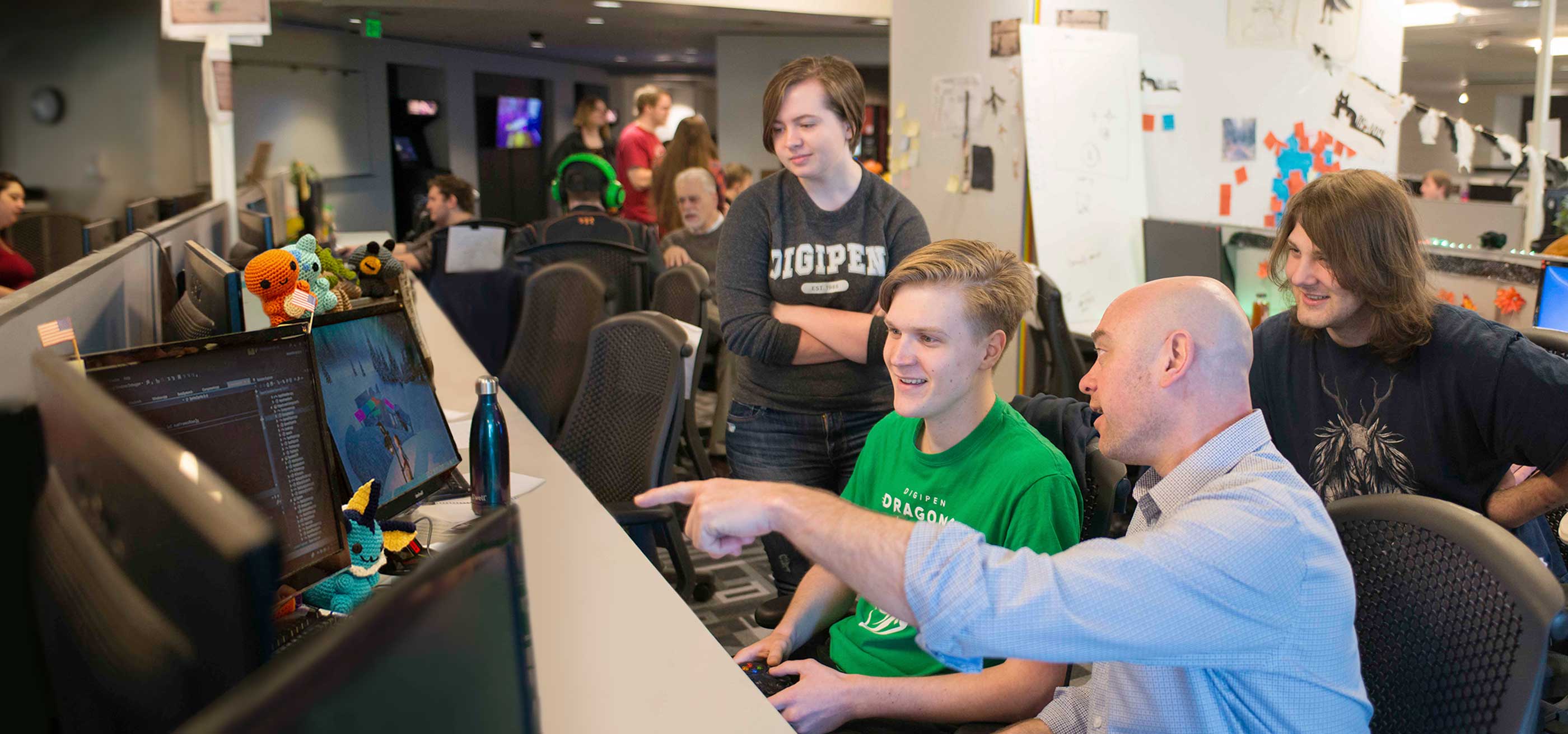 A DigiPen professor points to three students’ game team project on a computer in a campus production lab.