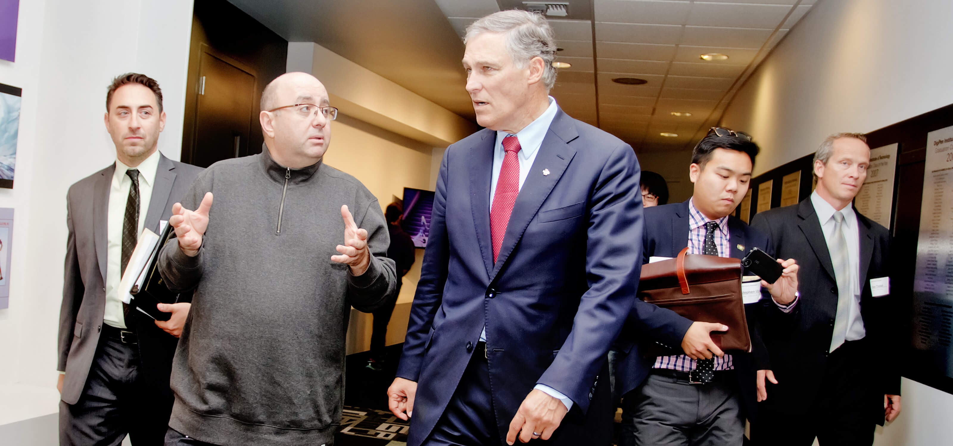 DigiPen founder Claude Comair and Washington Governor Jay Inslee walking down the hall surrounded by staffers