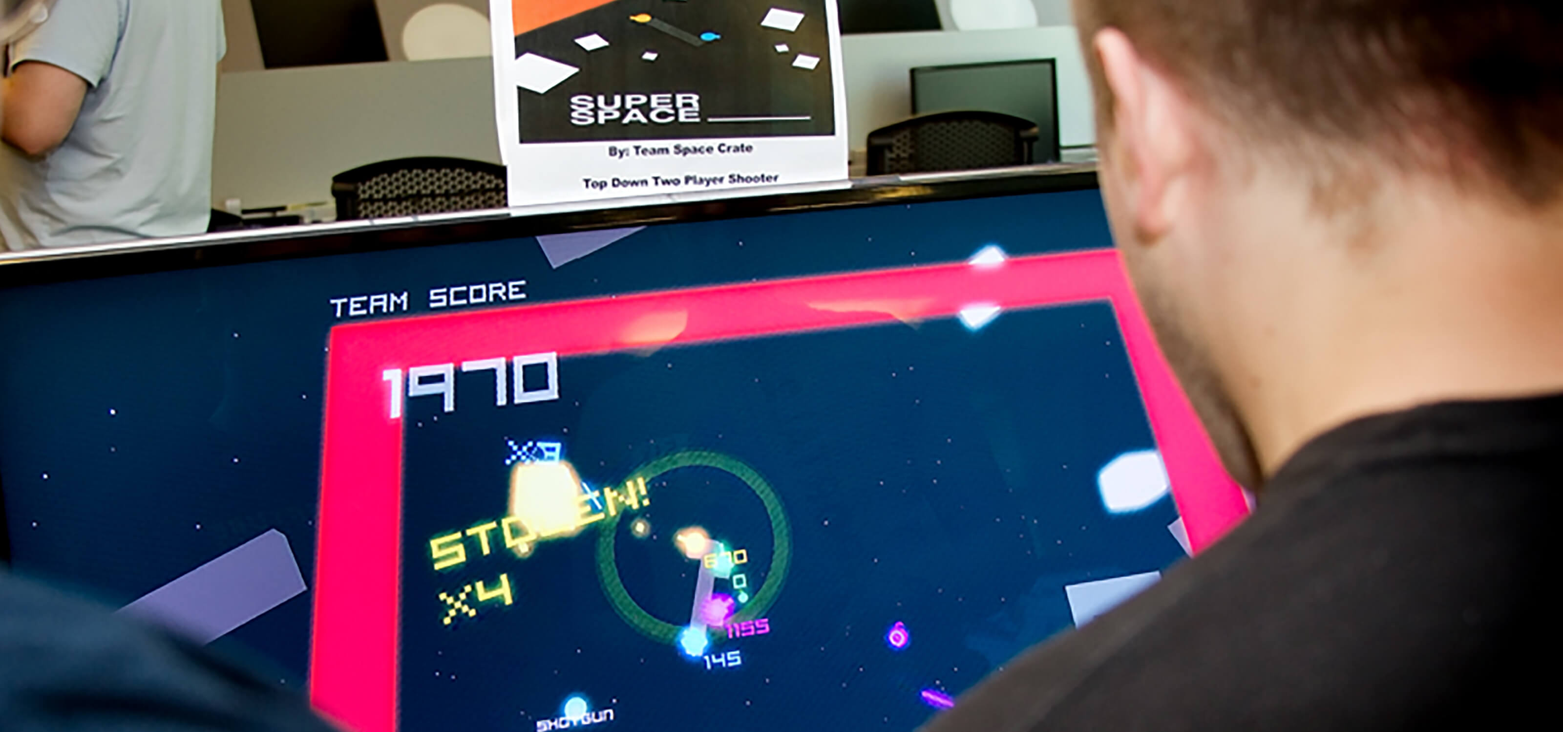 Over-the-shoulder view of two people playing the game Super Space ____; blocks and numbers float in space on a TV screen