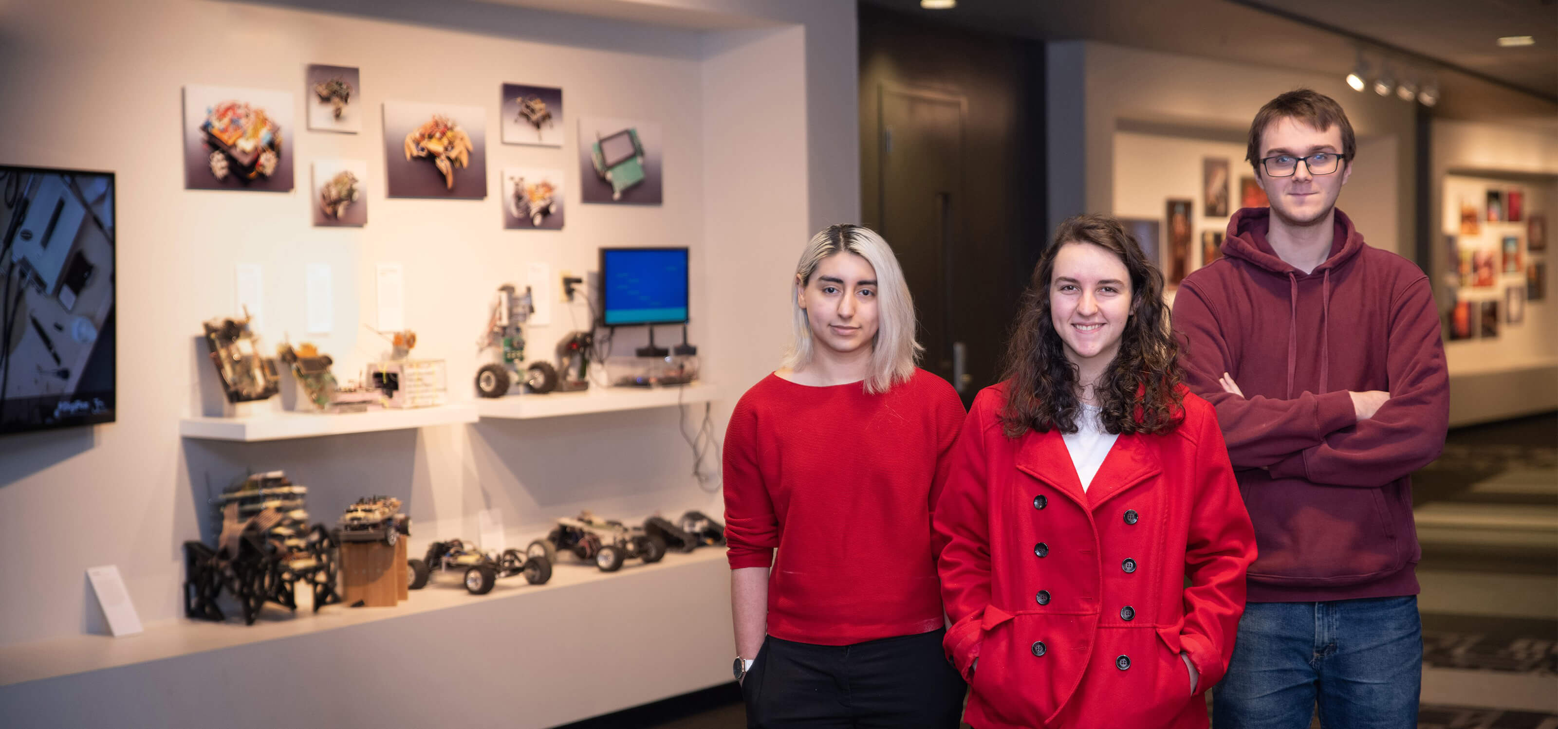 Three students stand next to computer engineering projects on display.