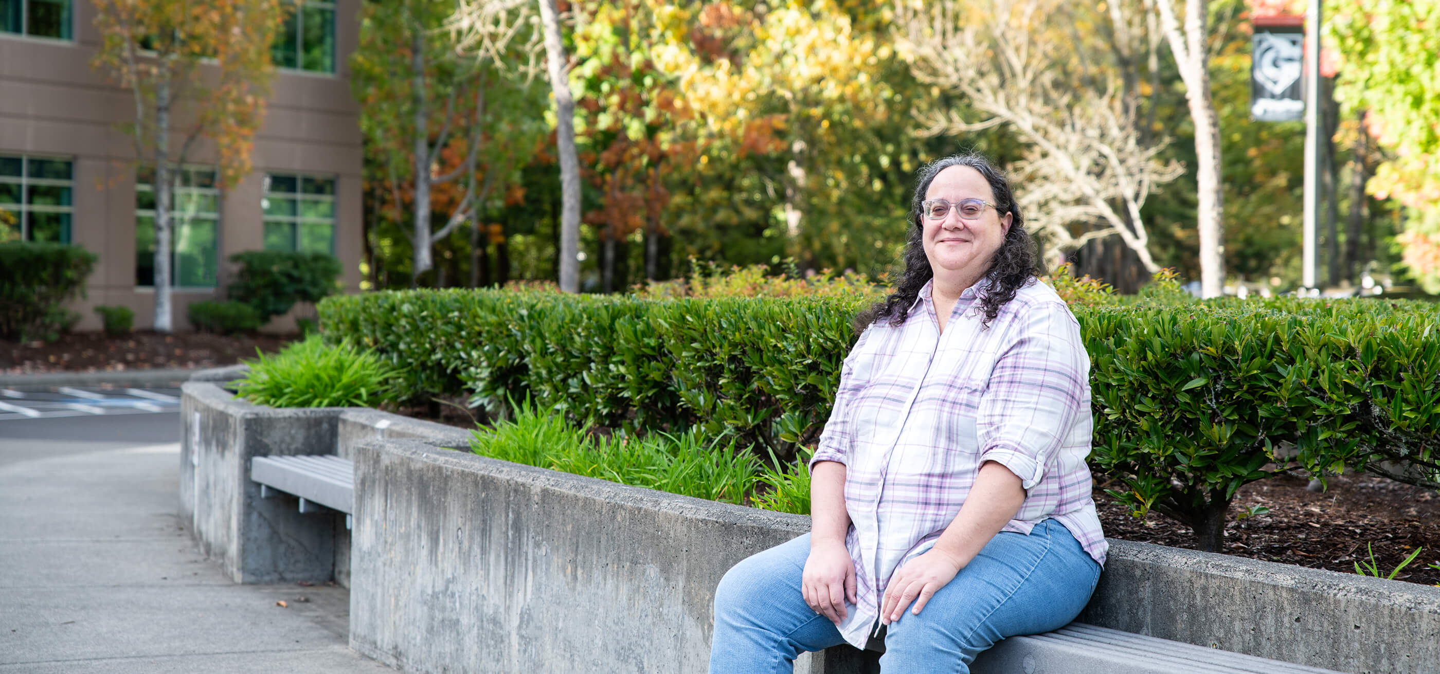 Ellen Beeman sits on a bench outside campus on a sunny day