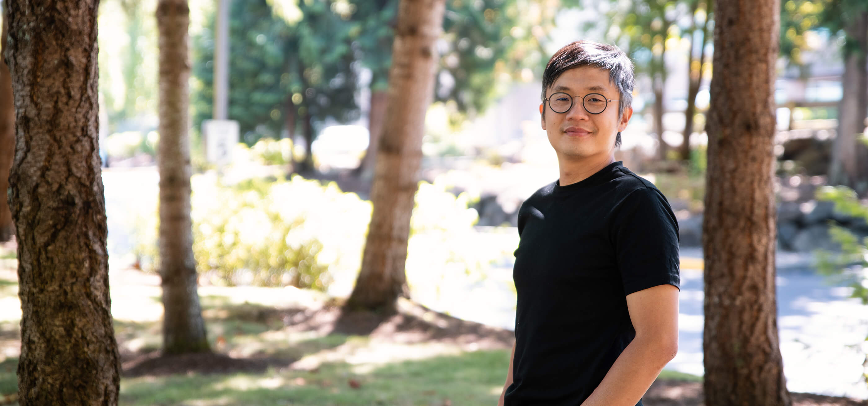 DigiPen instructor YZ Tan smiles with his hands in his pockets on a grassy, tree-filled lot.