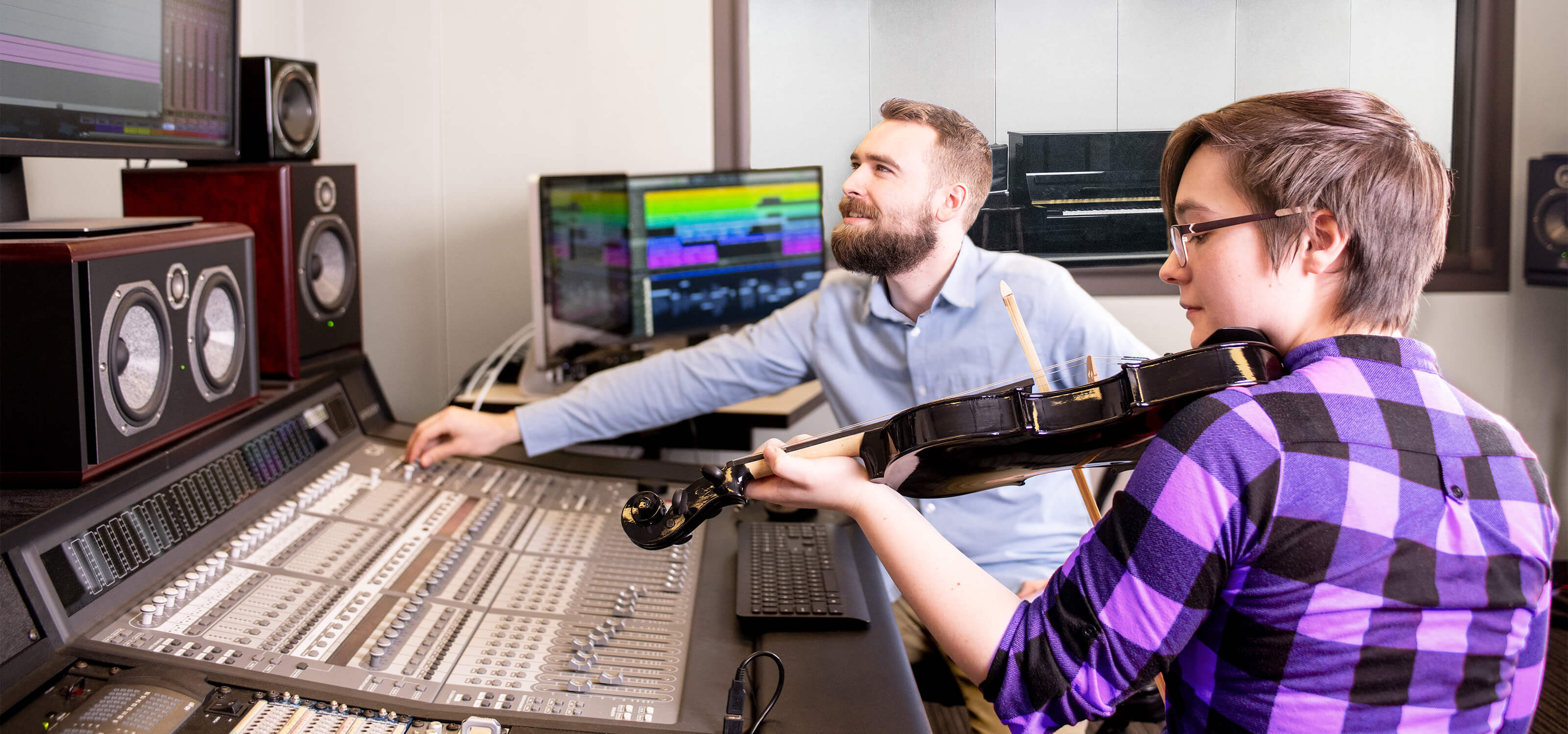 A DigiPen student plays violin next to a large audio mixing board.